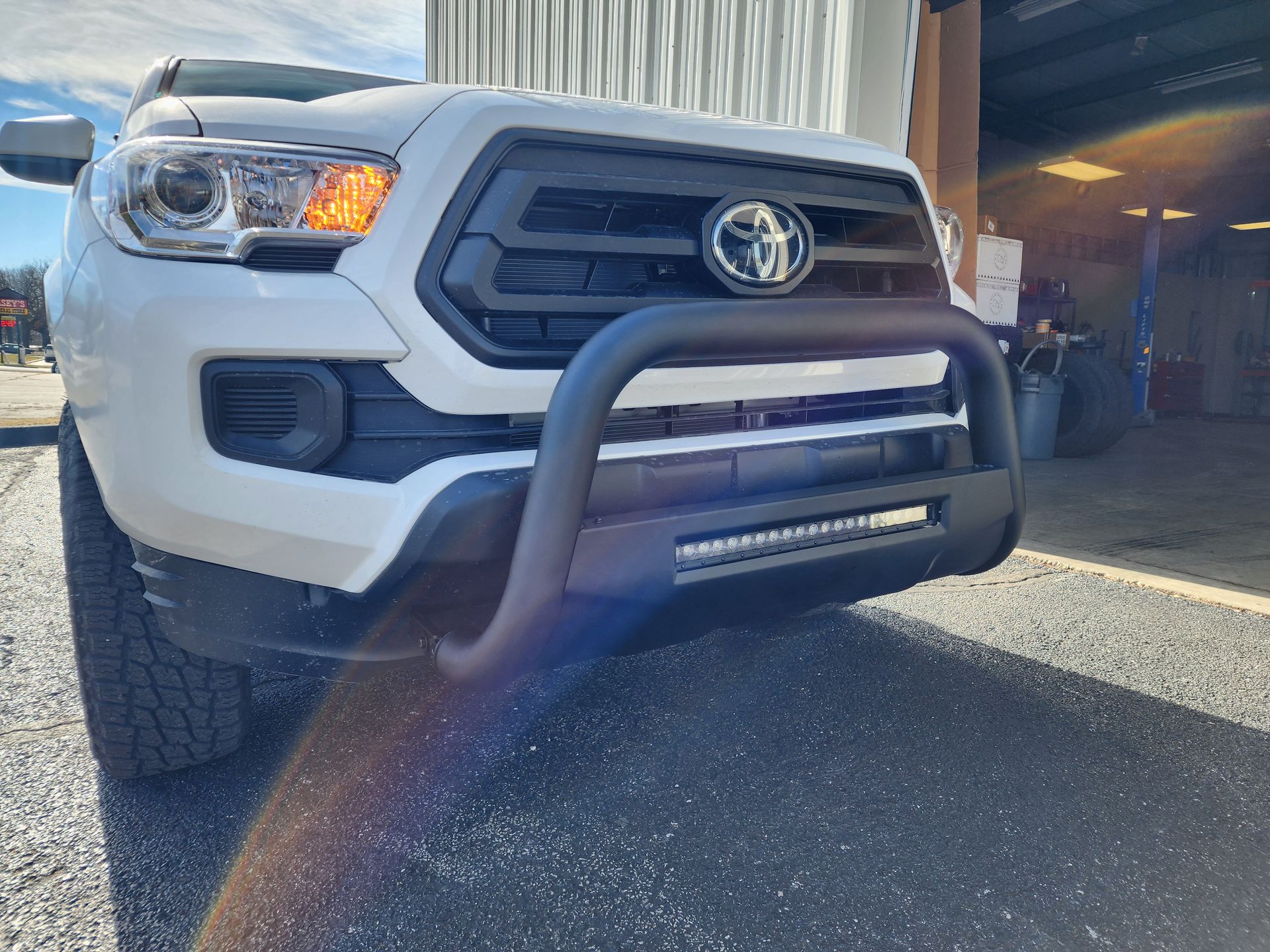 White pickup truck with black grille guard parked by a garage entrance in daylight