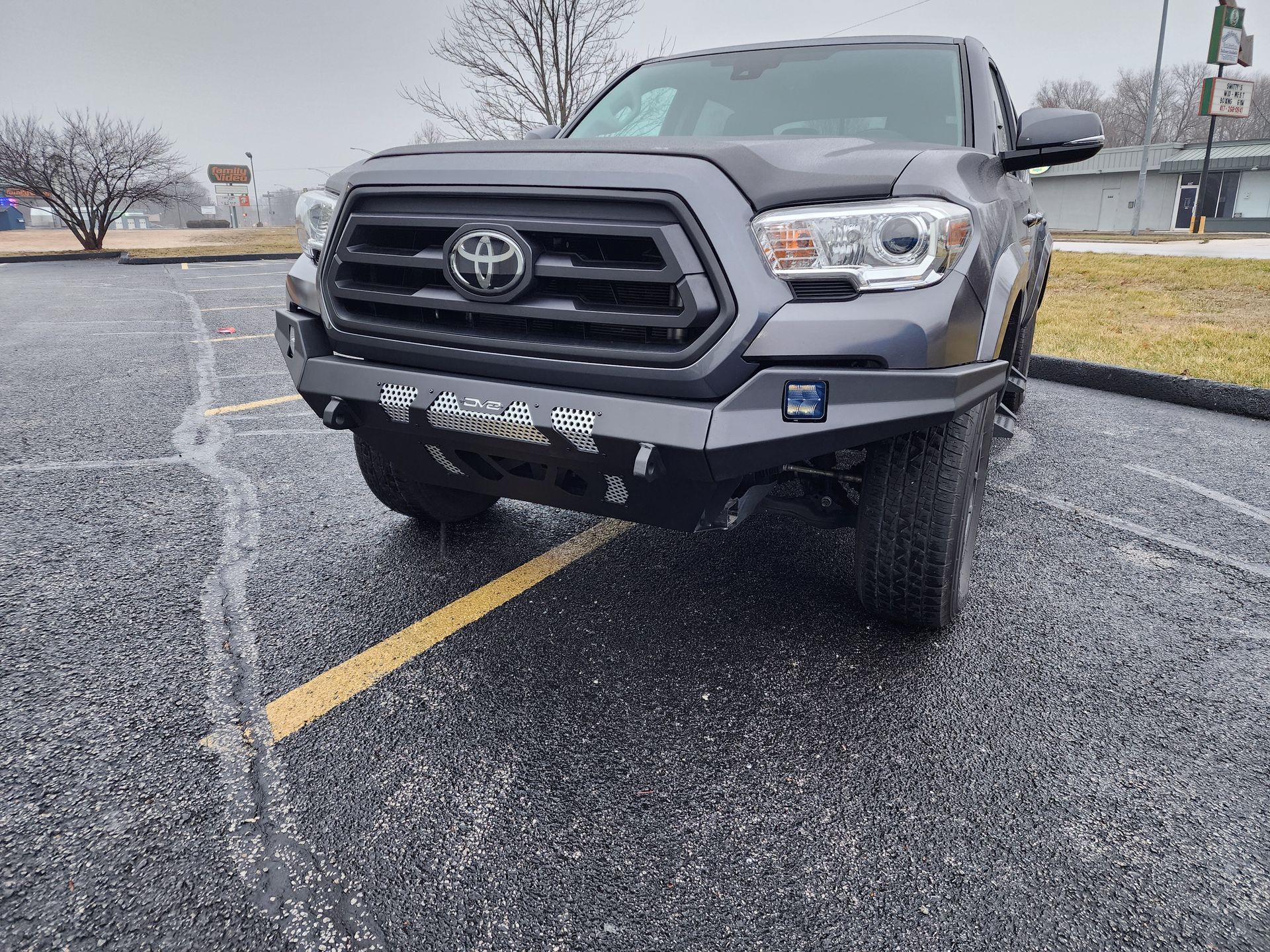 Front view of a gray Toyota truck parked on a wet asphalt lot in light snow.