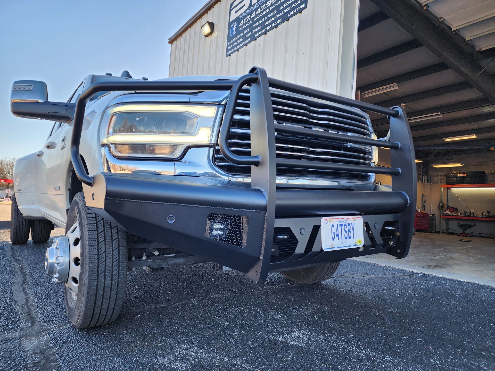Black pickup truck with chrome grille and bull bar parked beside an open garage.