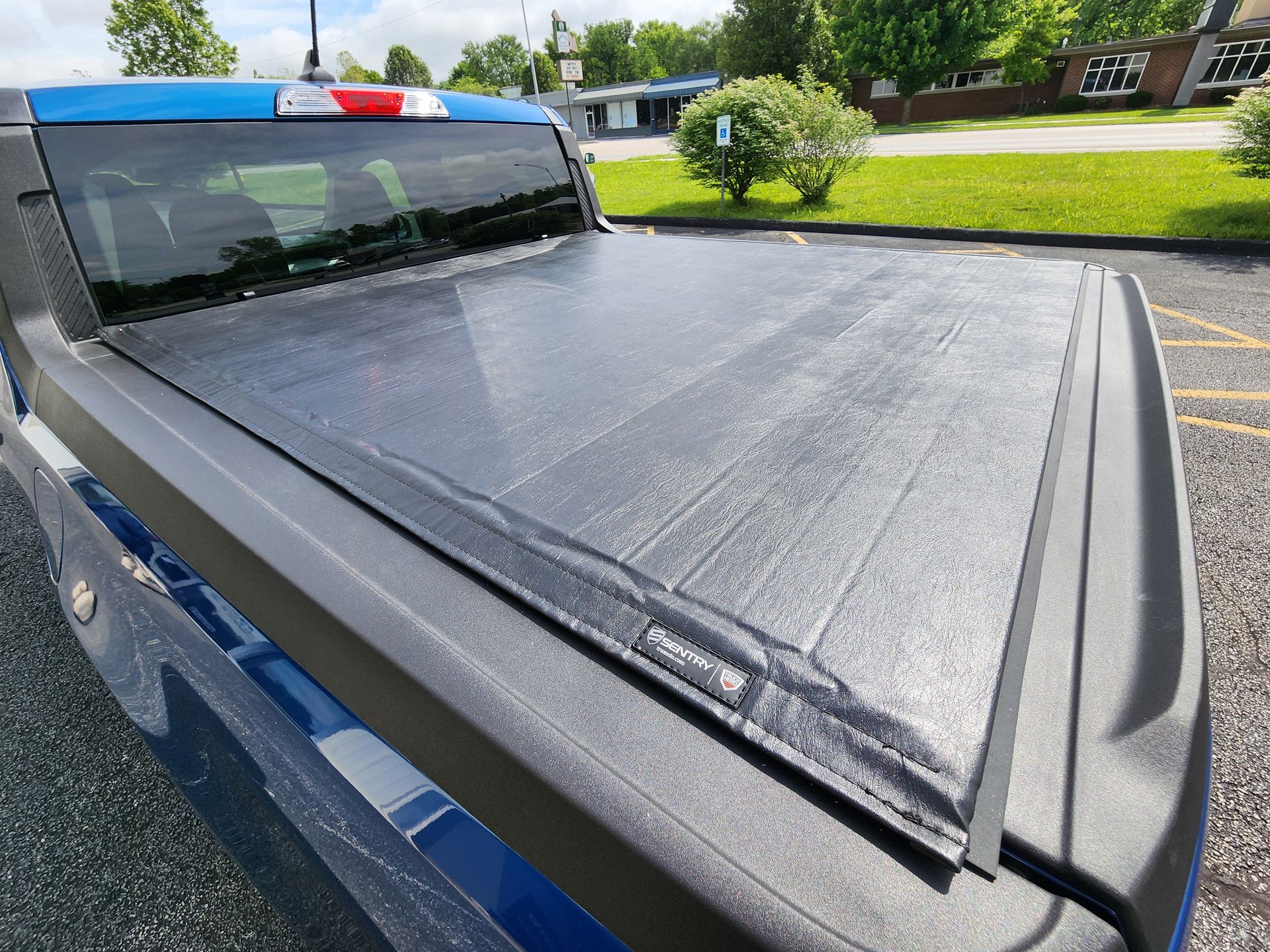 Black tonneau cover on a blue pickup truck parked outdoors in daylight