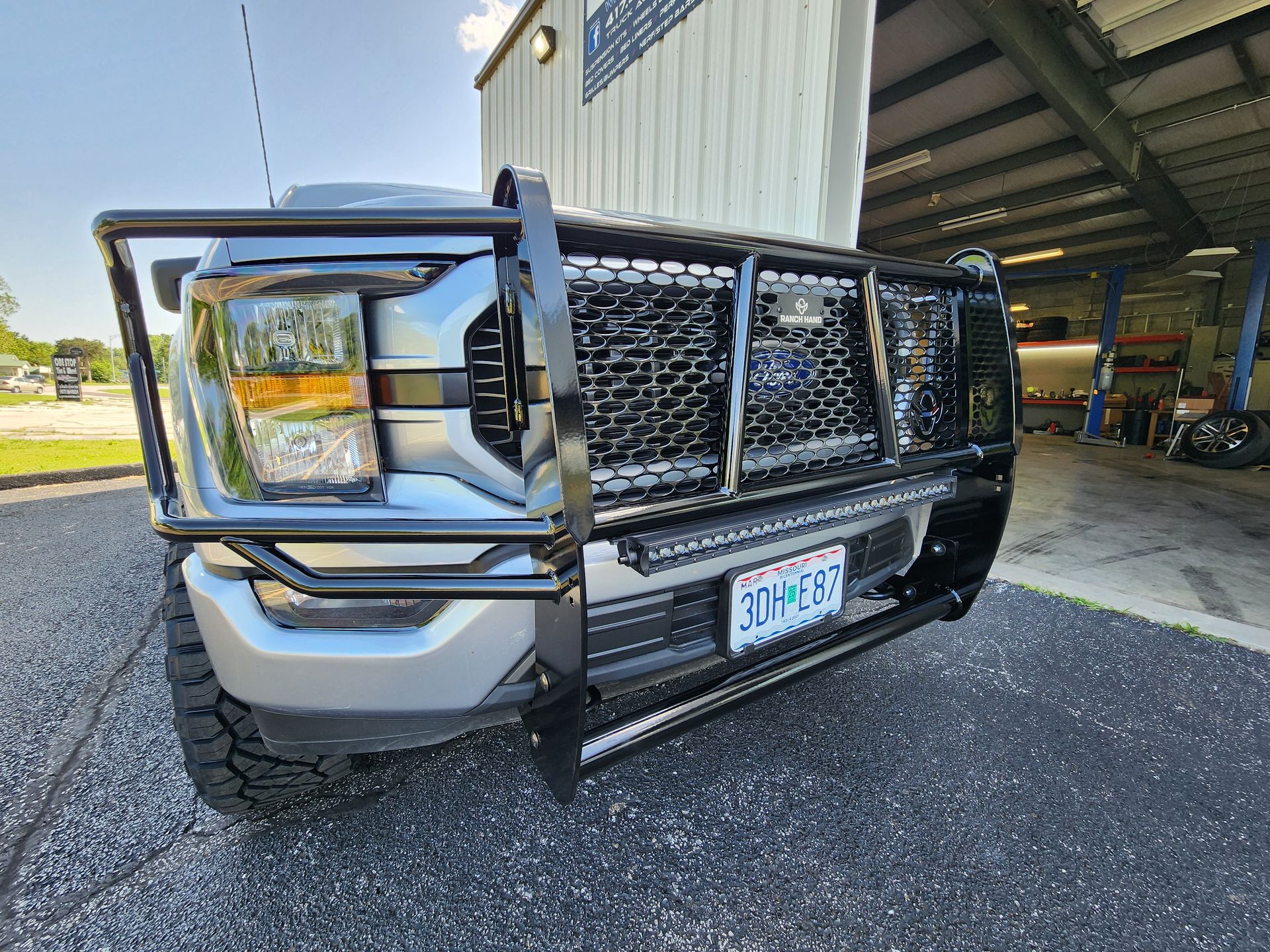 Silver pickup truck with black grille guard parked outside a building
