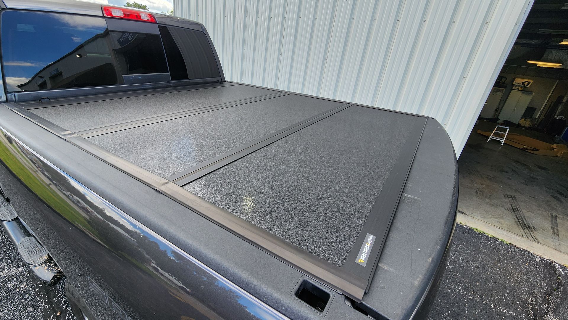Black pickup truck bed cover covered in water droplets beside a white building