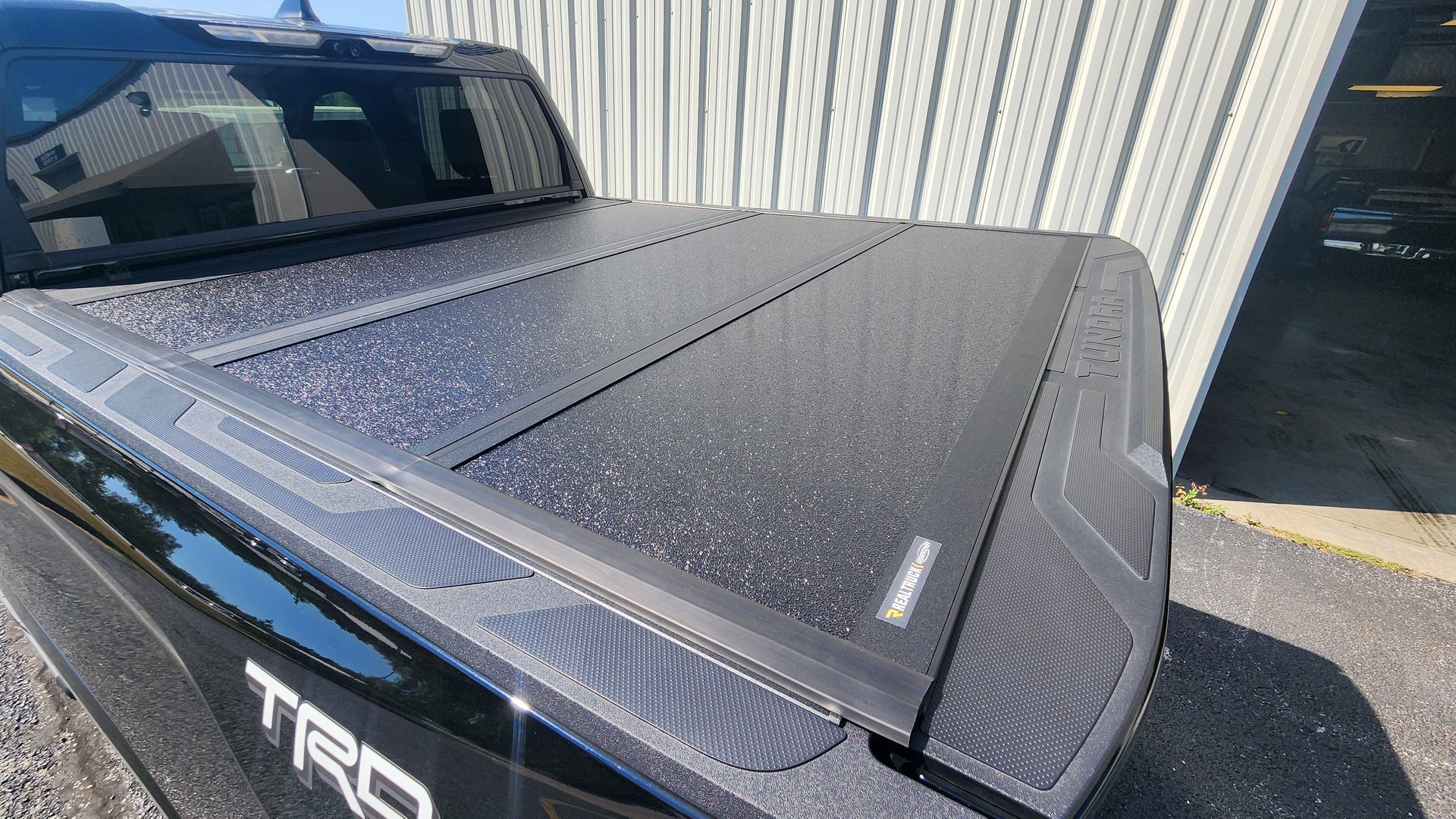 Black Toyota truck bed cover with water droplets beside a corrugated metal building