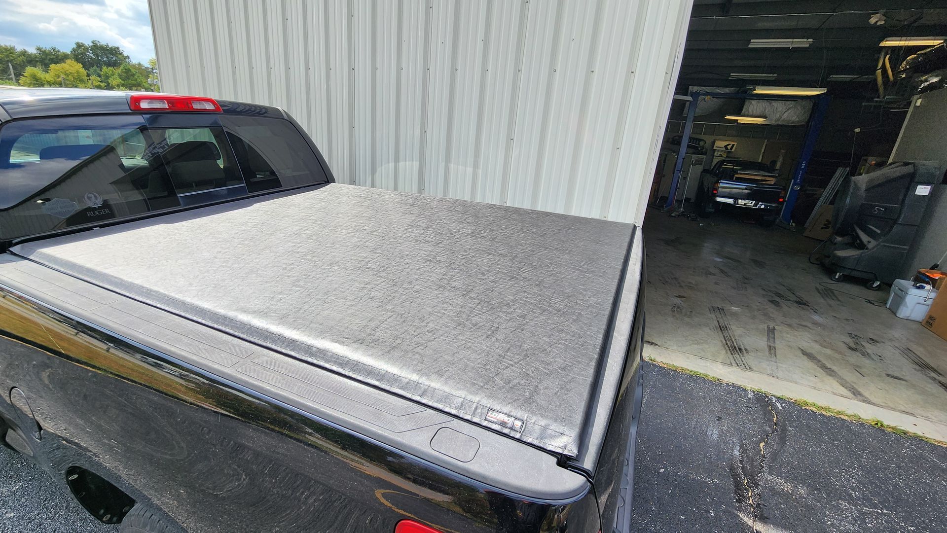 Black pickup truck bed cover partially closed beside a garage entrance.