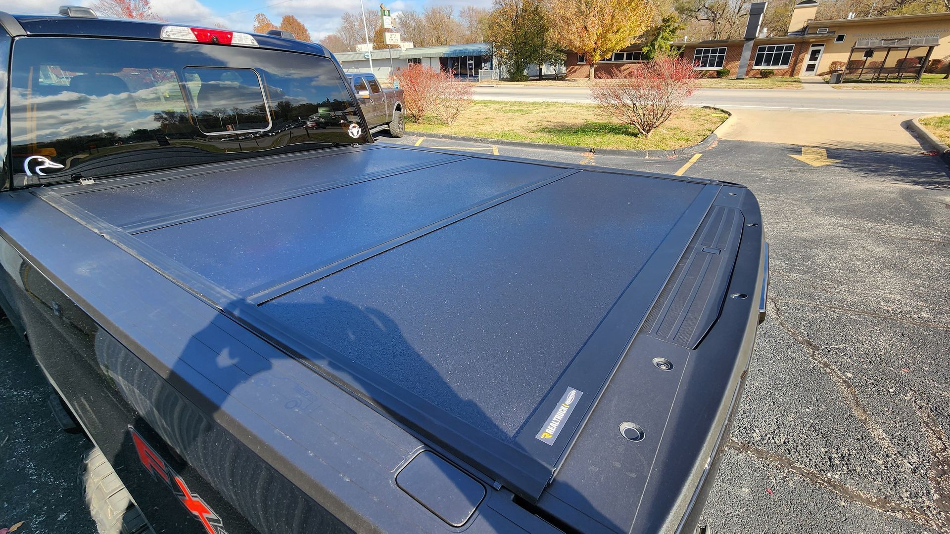 Black pickup truck with a hard tonneau cover parked outdoors on a sunny day.