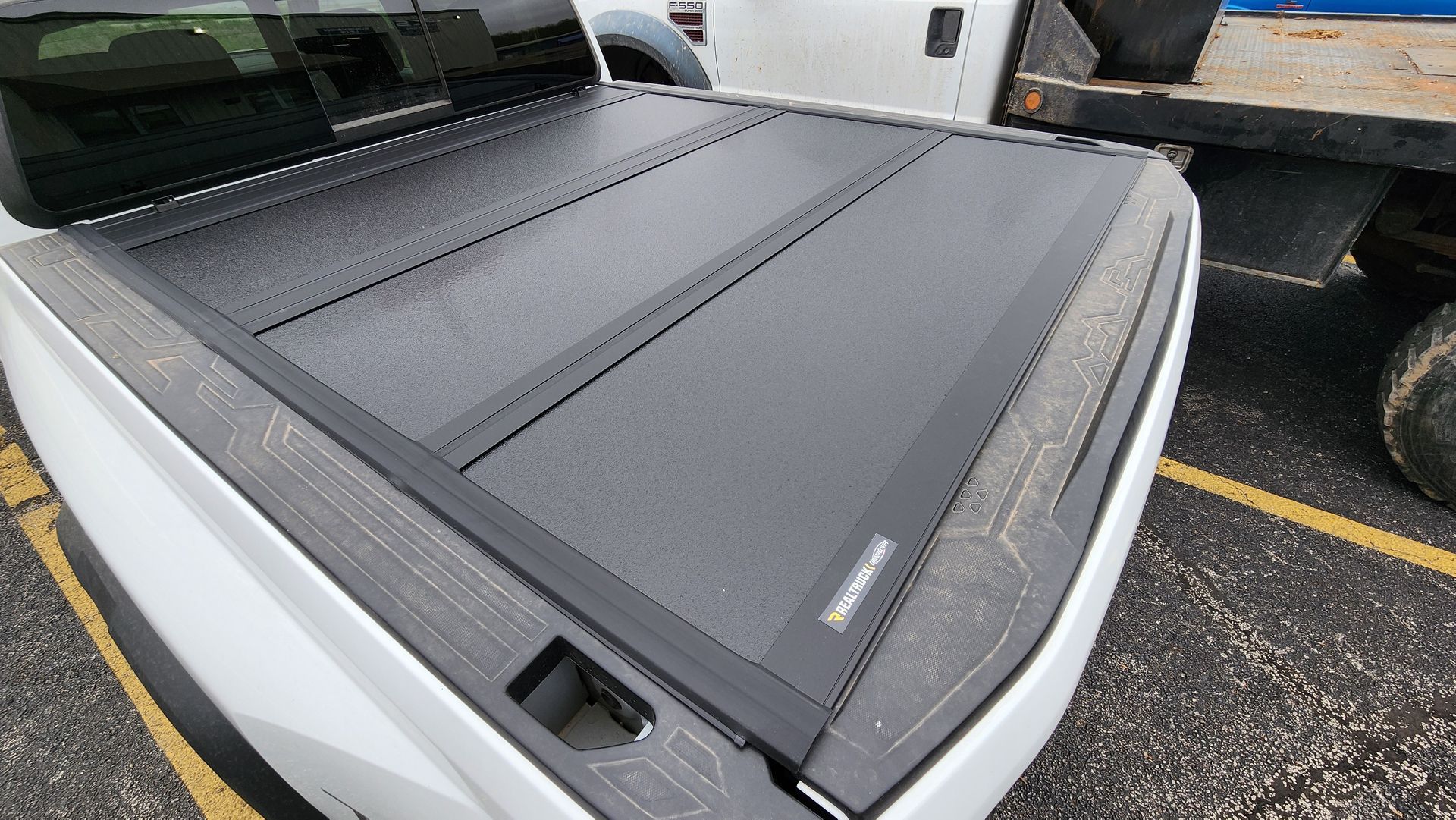 Black folding truck bed tonneau cover on a pickup in a parking lot.