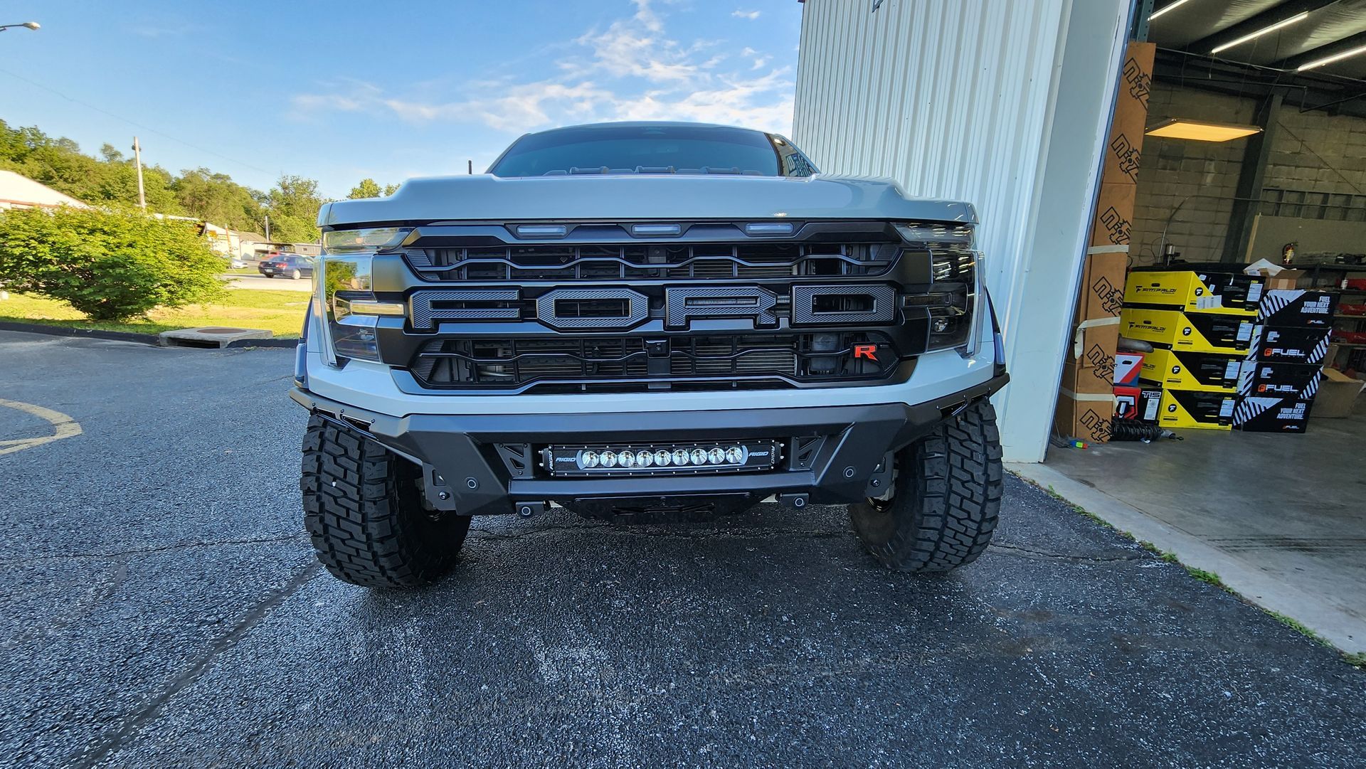 Front view of a black pickup truck parked beside a building on a gravel driveway.