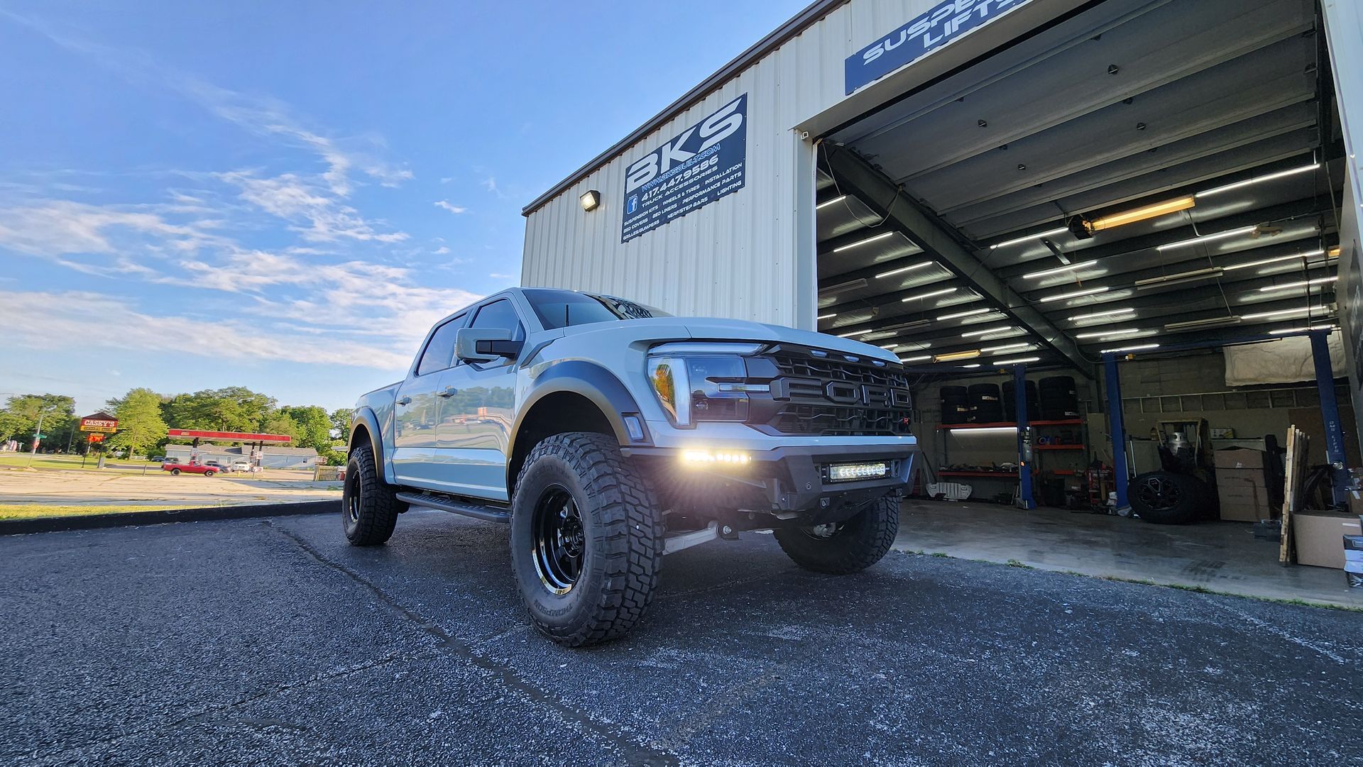 Silver pickup truck parked beside an open garage at a warehouse, viewed from a low angle