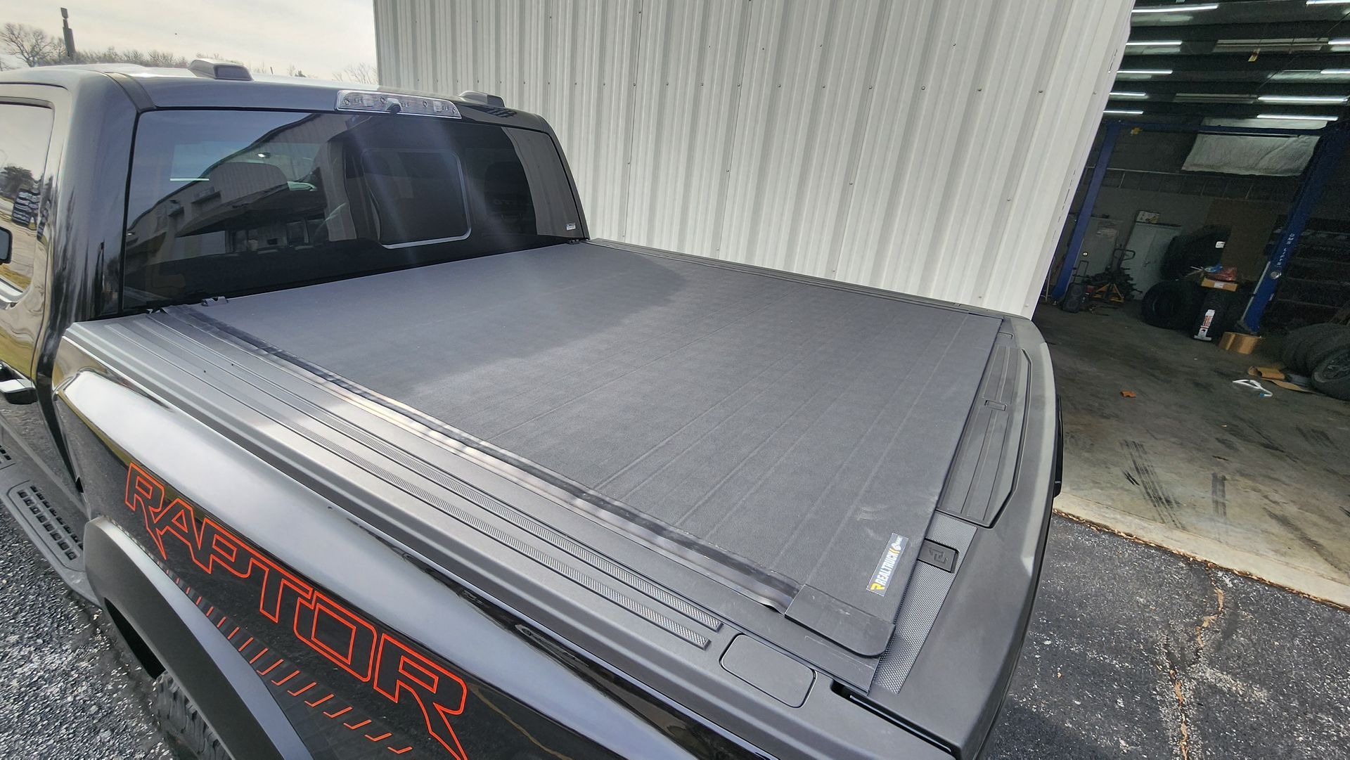 Gray pickup truck with a black soft bed cover parked beside a garage opening
