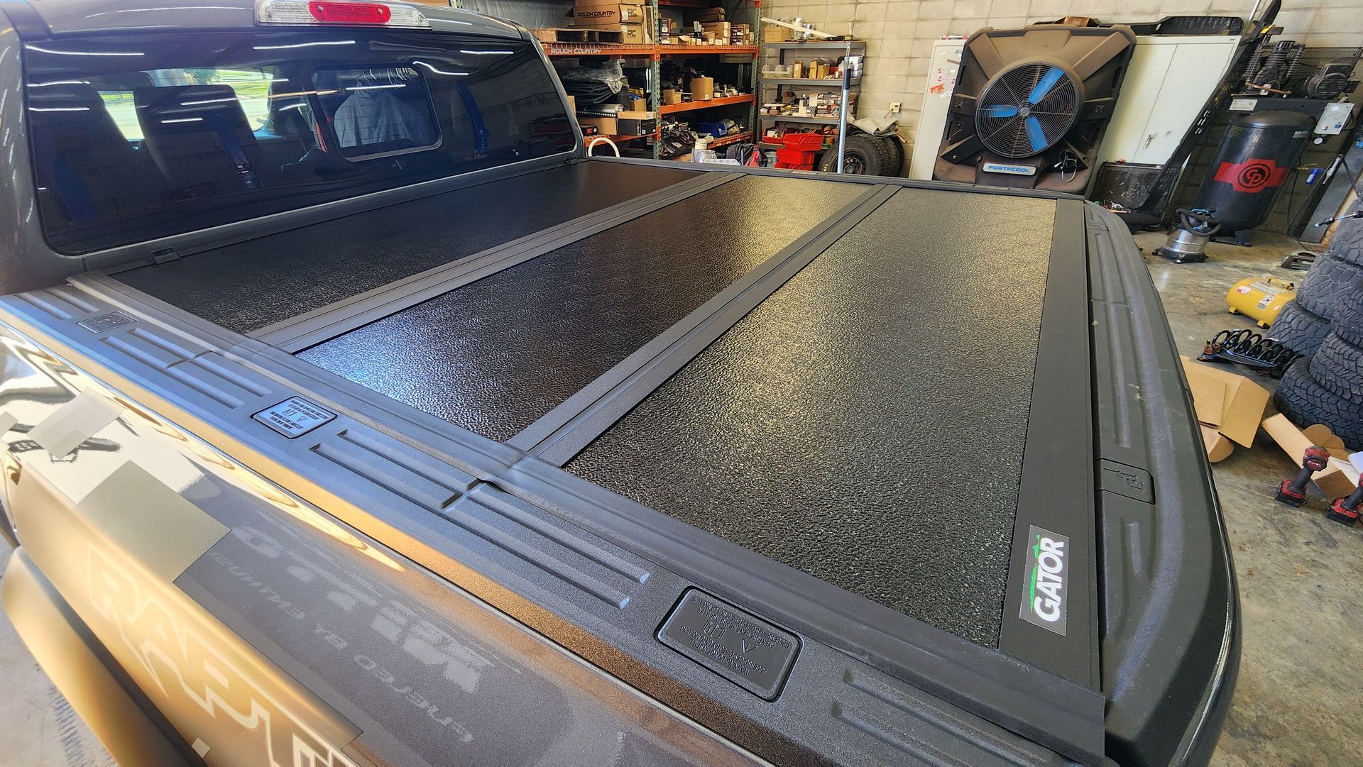 Black pickup truck with a textured tonneau cover in a garage or workshop setting