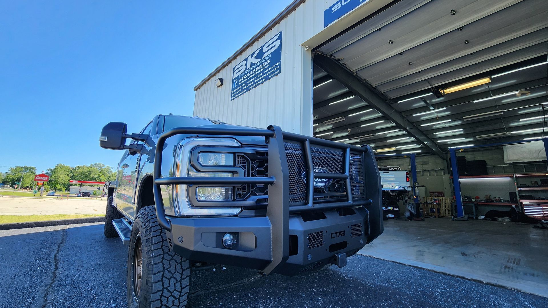 Blue lifted truck parked outside an open garage bay on a sunny day