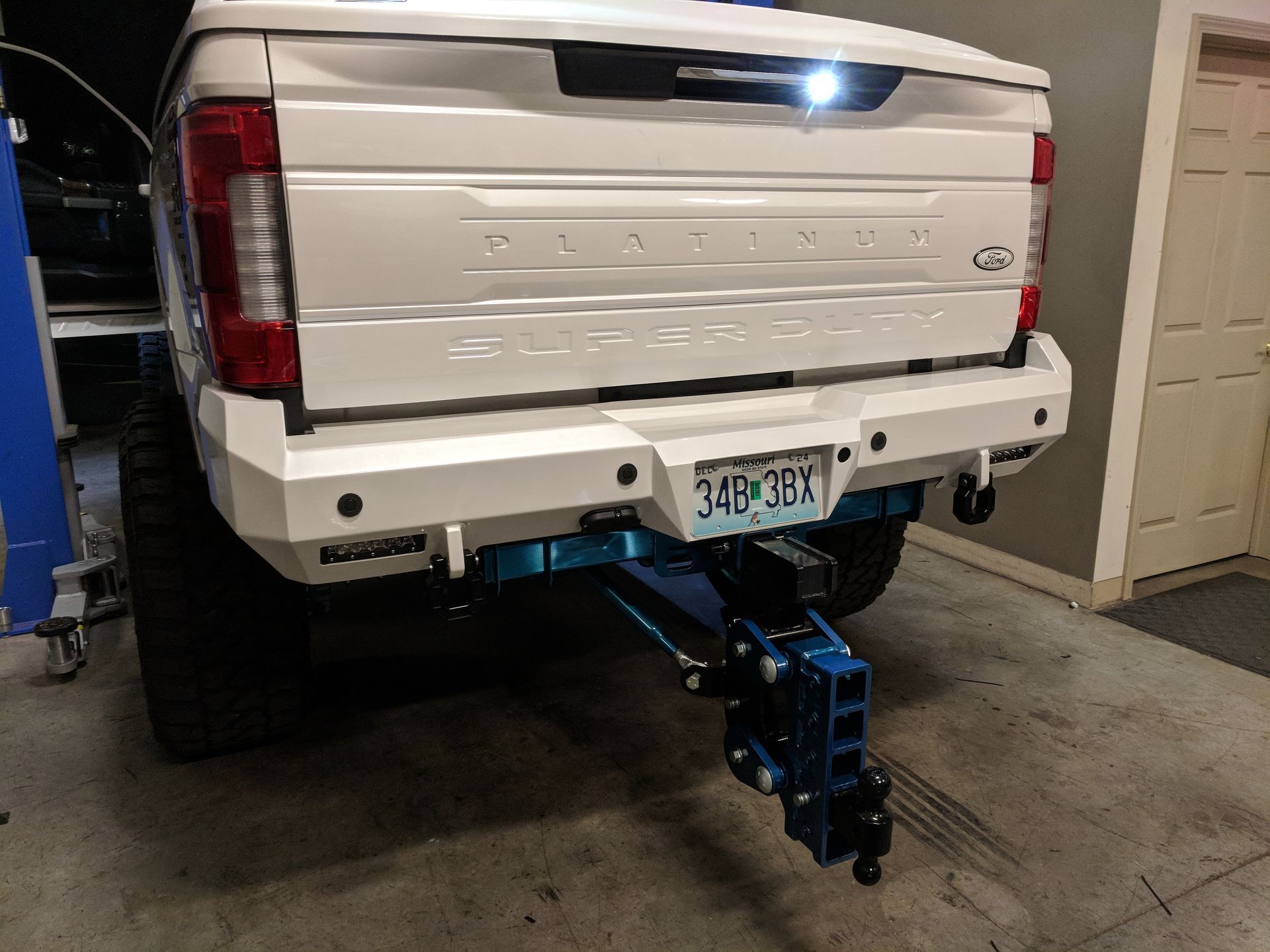 White pickup truck with rear hitch-mounted tow accessory in a garage, rear view