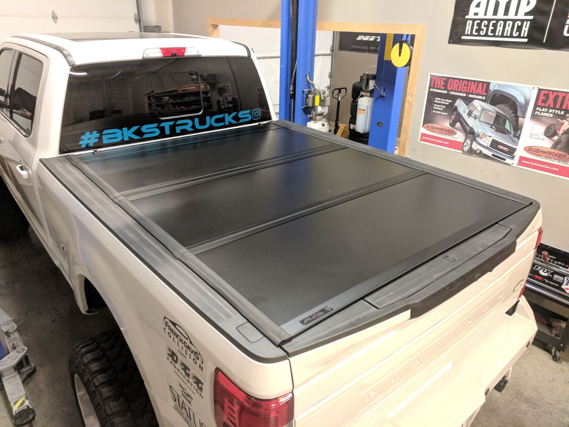 Black pickup truck with a hard tonneau cover in a garage, viewed from the rear corner