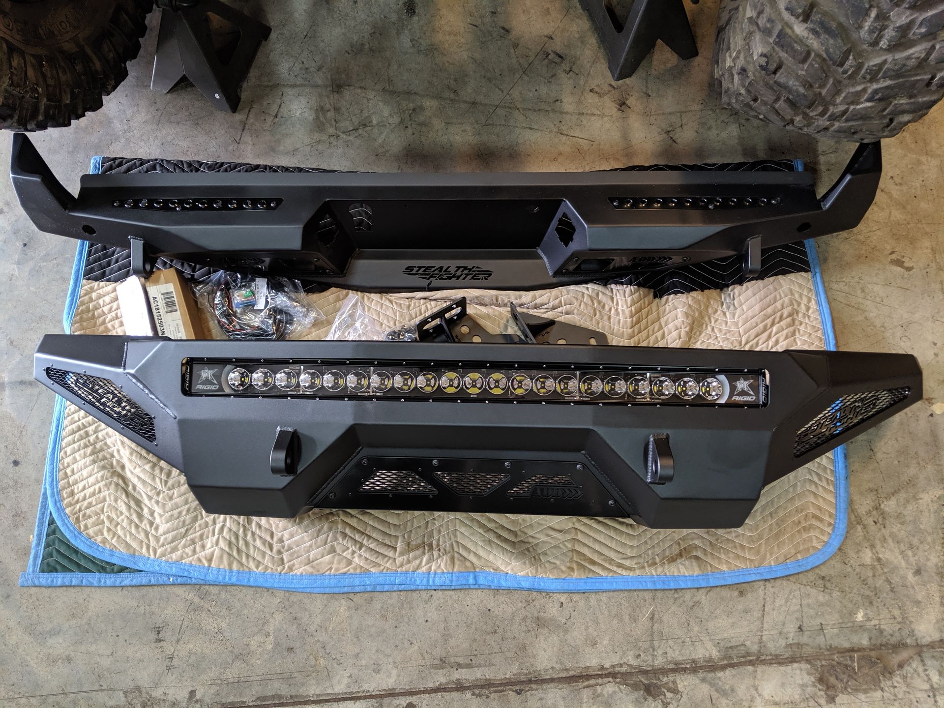 Two black off-road vehicle bumpers with LED light bars on a garage floor