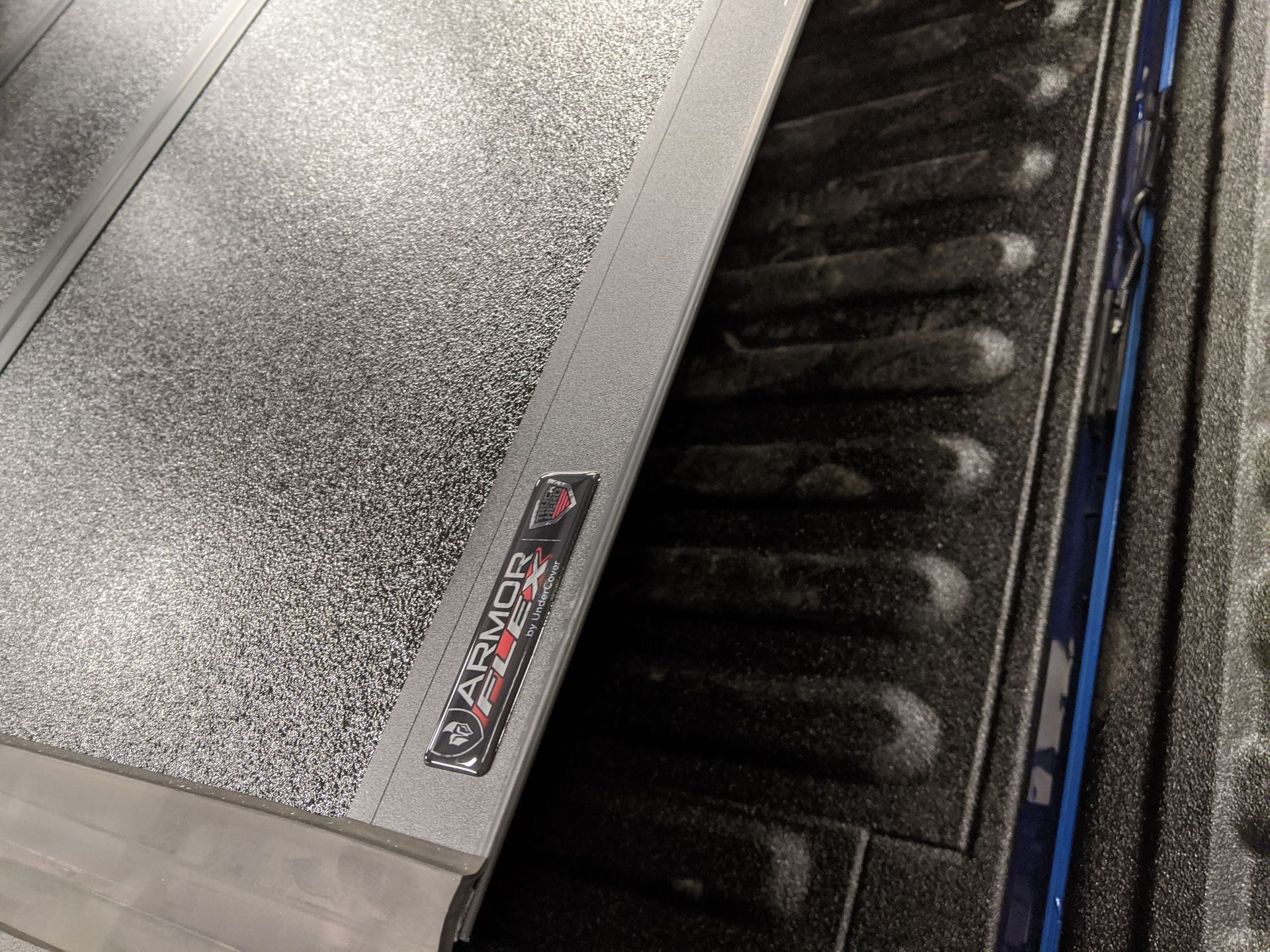 Close-up of a black truck bed liner with a silver textured cover and metal rail edge