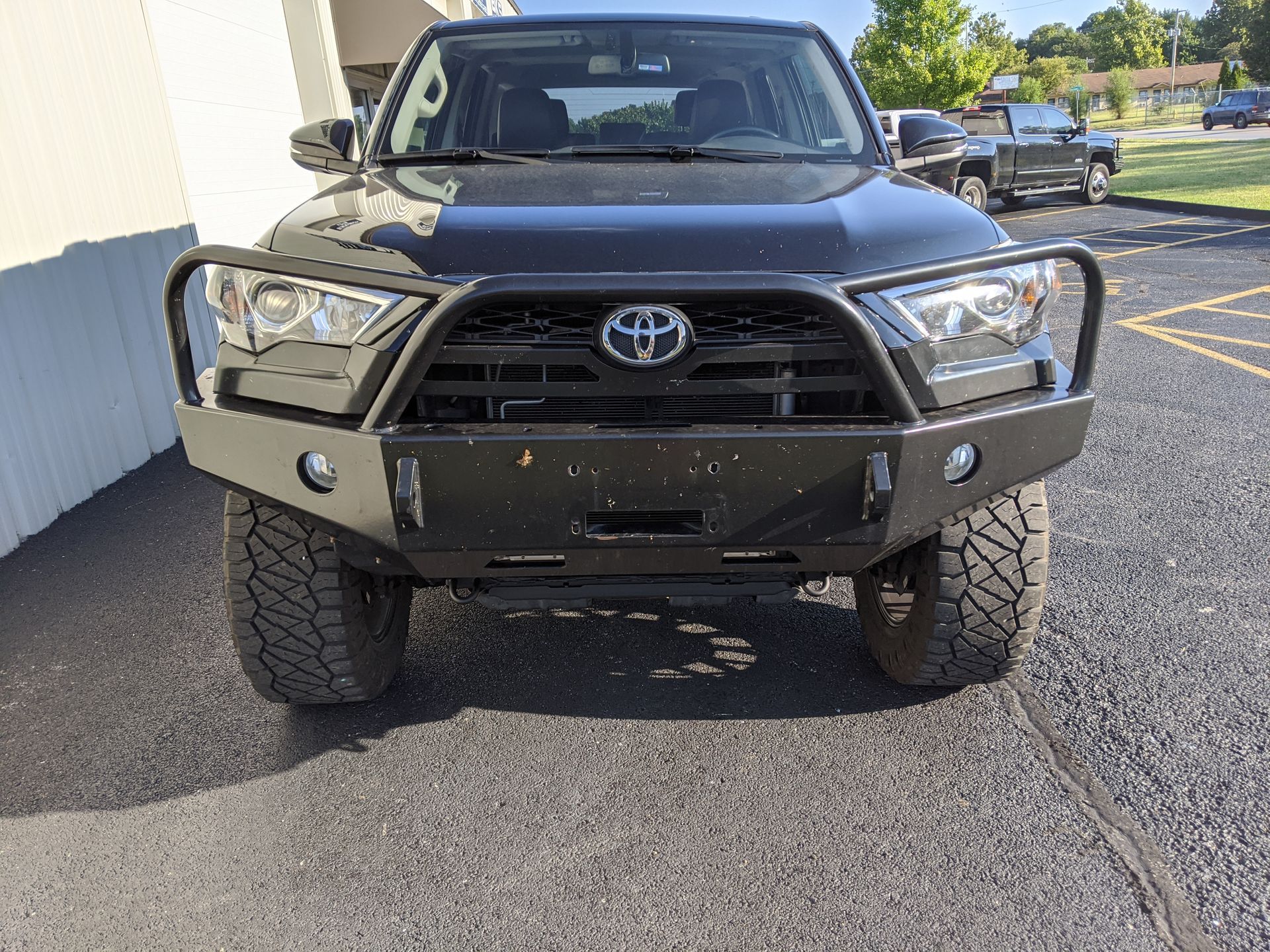 Black Toyota truck with off-road bumper parked on asphalt beside a building.