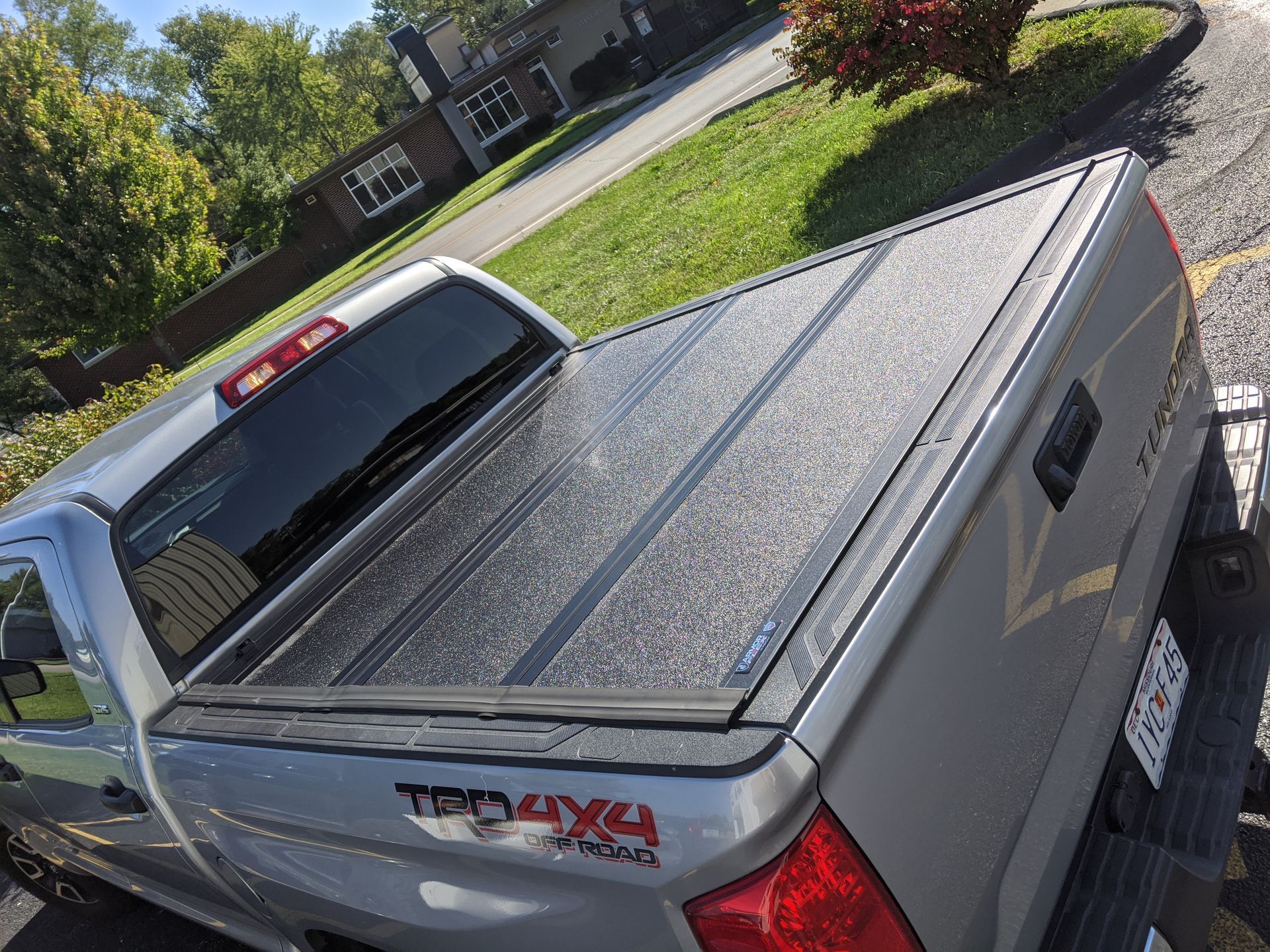 Silver pickup truck with a black tonneau cover parked in a driveway on a sunny day