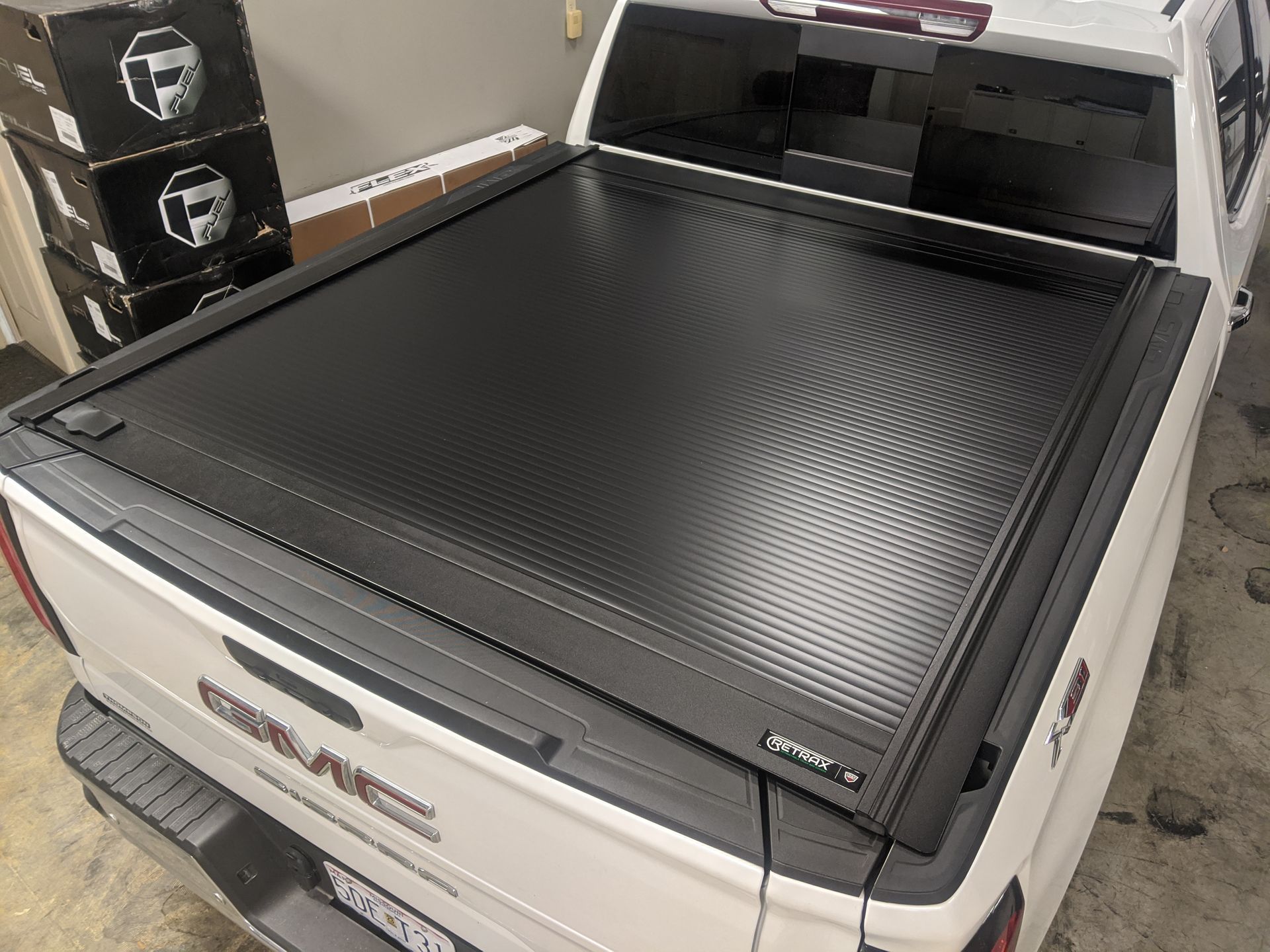 Black rolled-up tonneau cover on a white pickup truck in a garage.