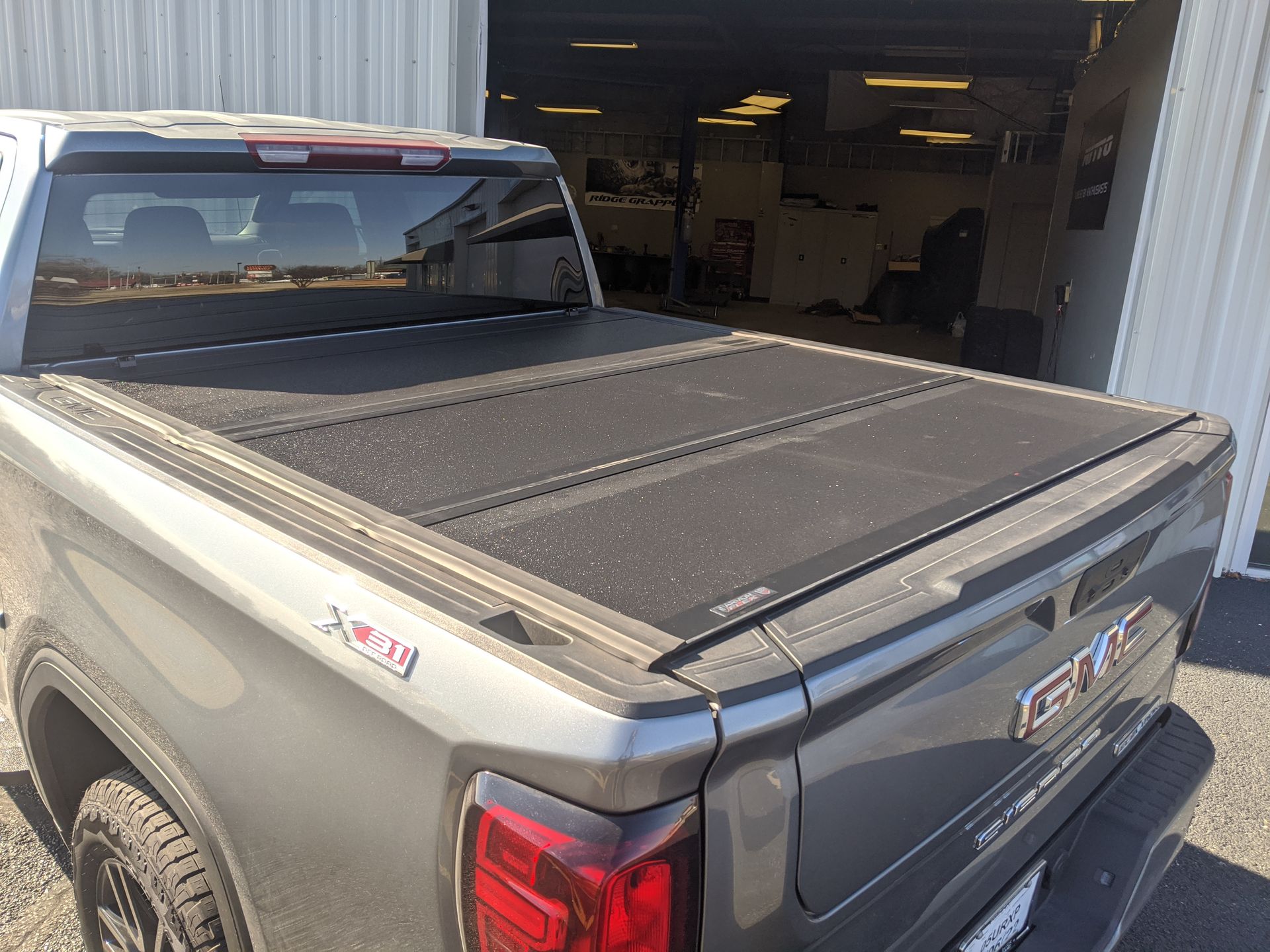 Gray pickup truck with a black tonneau cover parked at an auto shop bay entrance