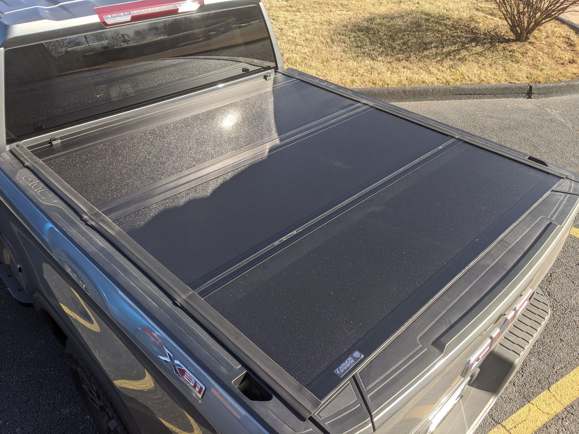 Black retractable bed cover on a blue pickup truck in a sunny parking lot