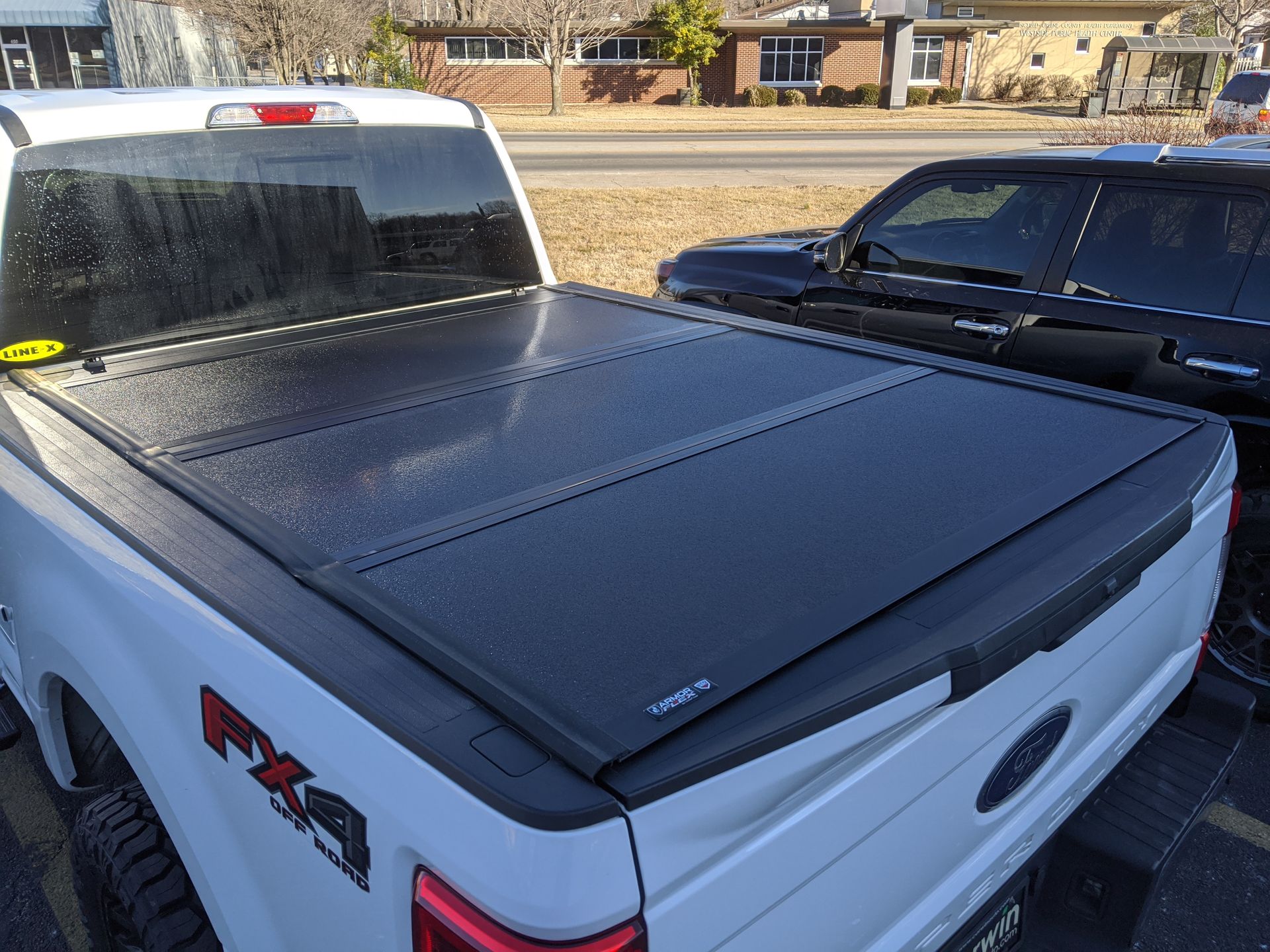White pickup truck with a black tonneau cover parked beside a dark SUV in a driveway