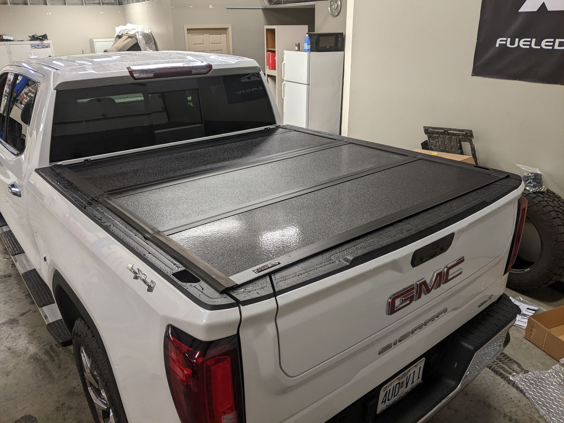White pickup truck with a black tonneau cover parked inside a garage.