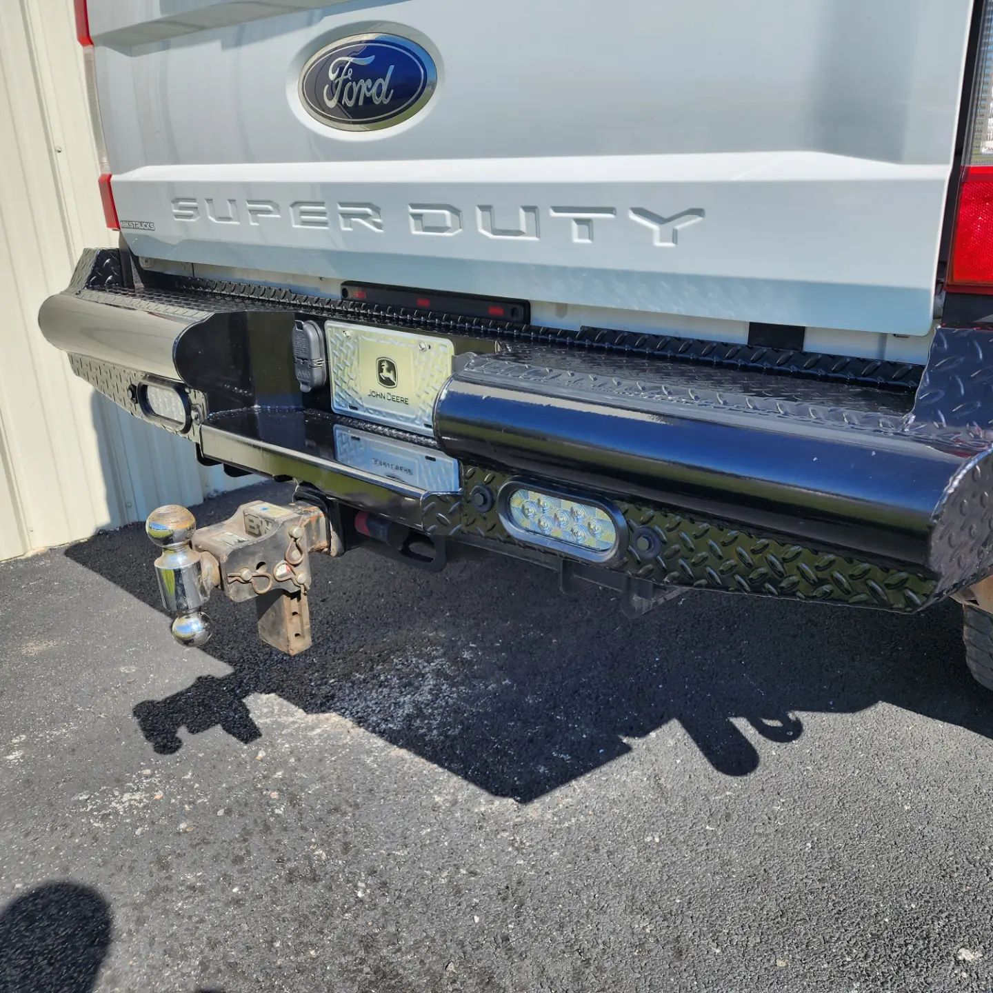 Rear of a Ford Super Duty truck with a trailer hitch and step bumper, parked on pavement.