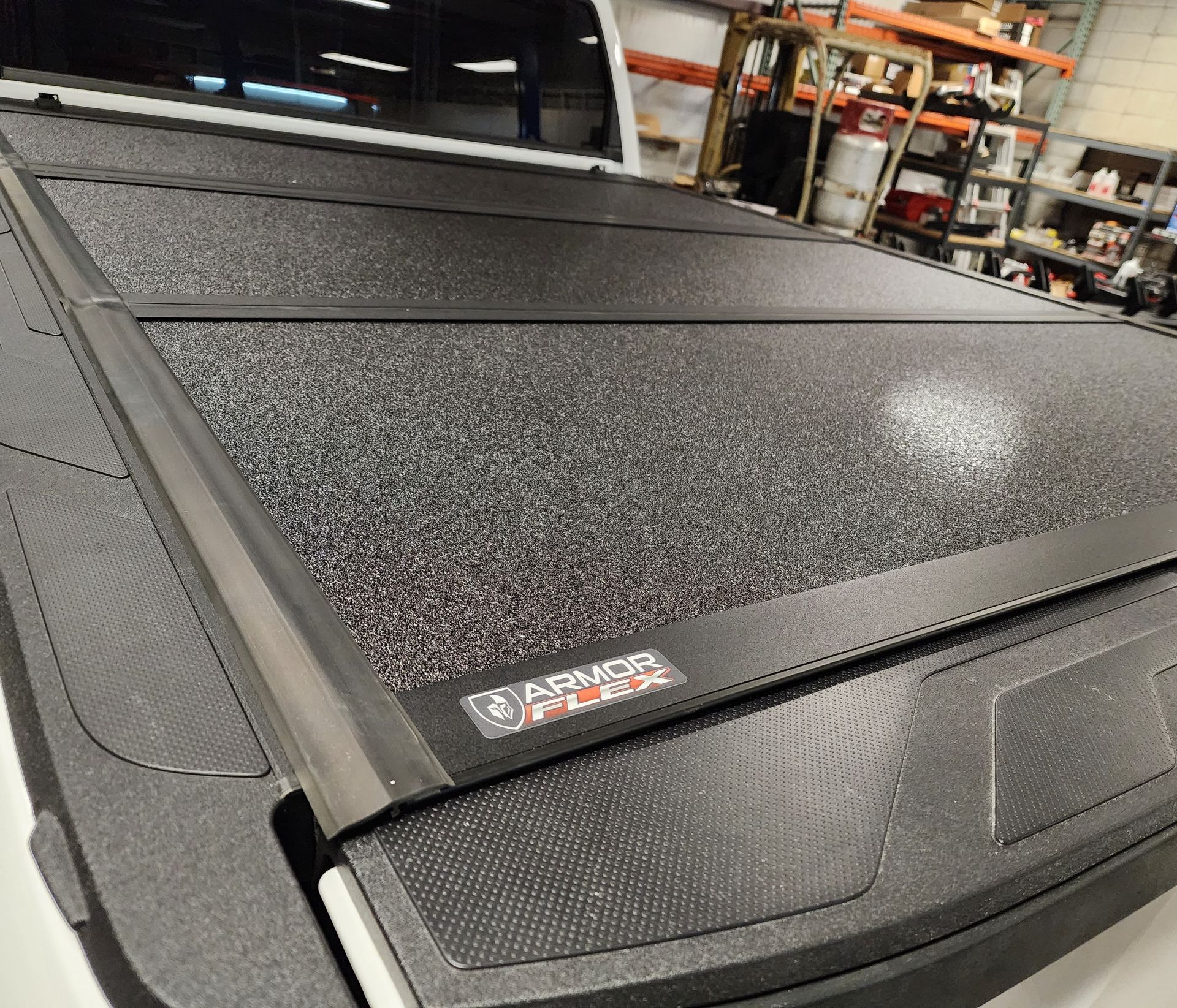 Textured black hard-shell truck bed cover in a workshop, angled close-up.
