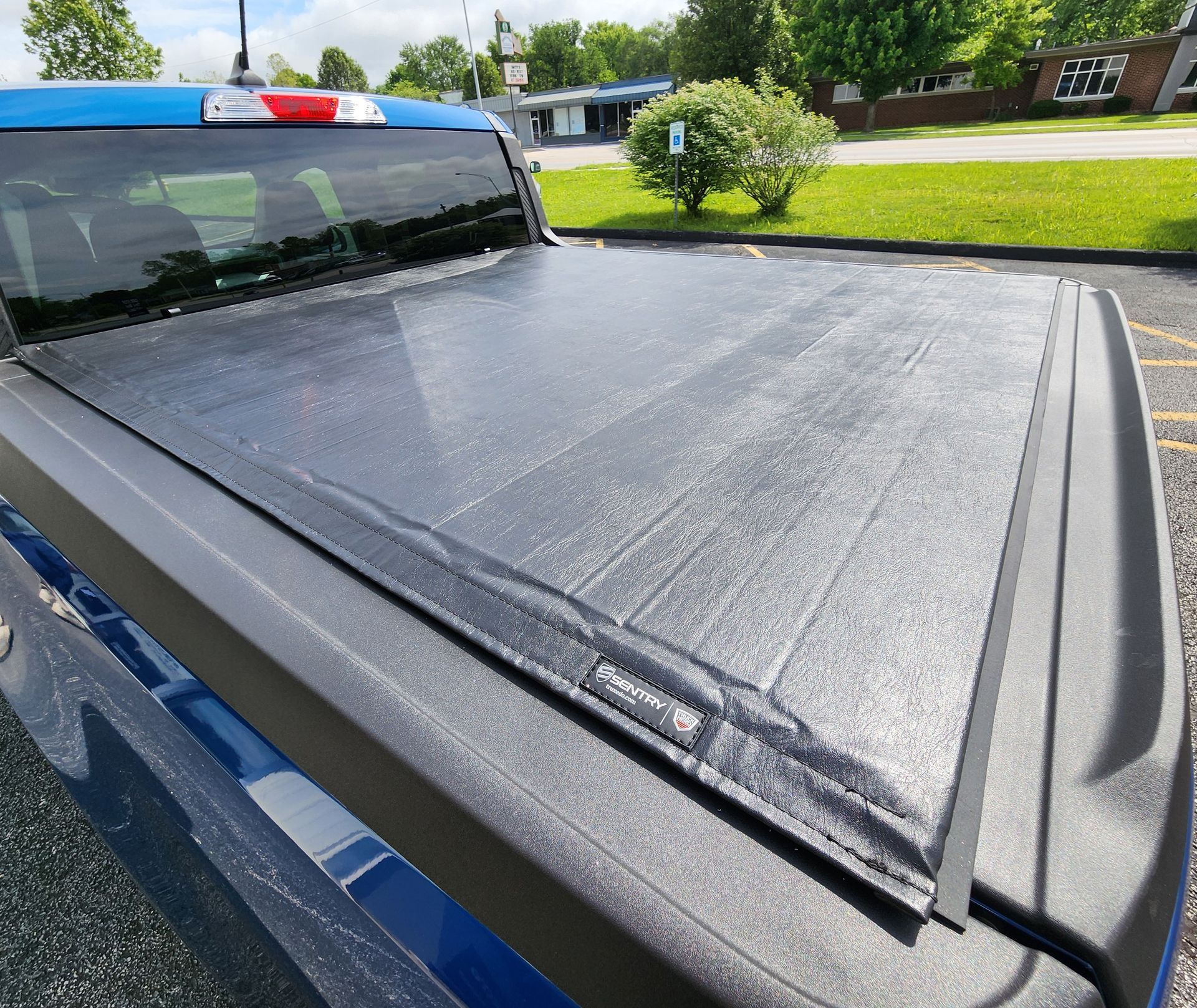 Closed black tonneau cover on the bed of a blue pickup truck outdoors.