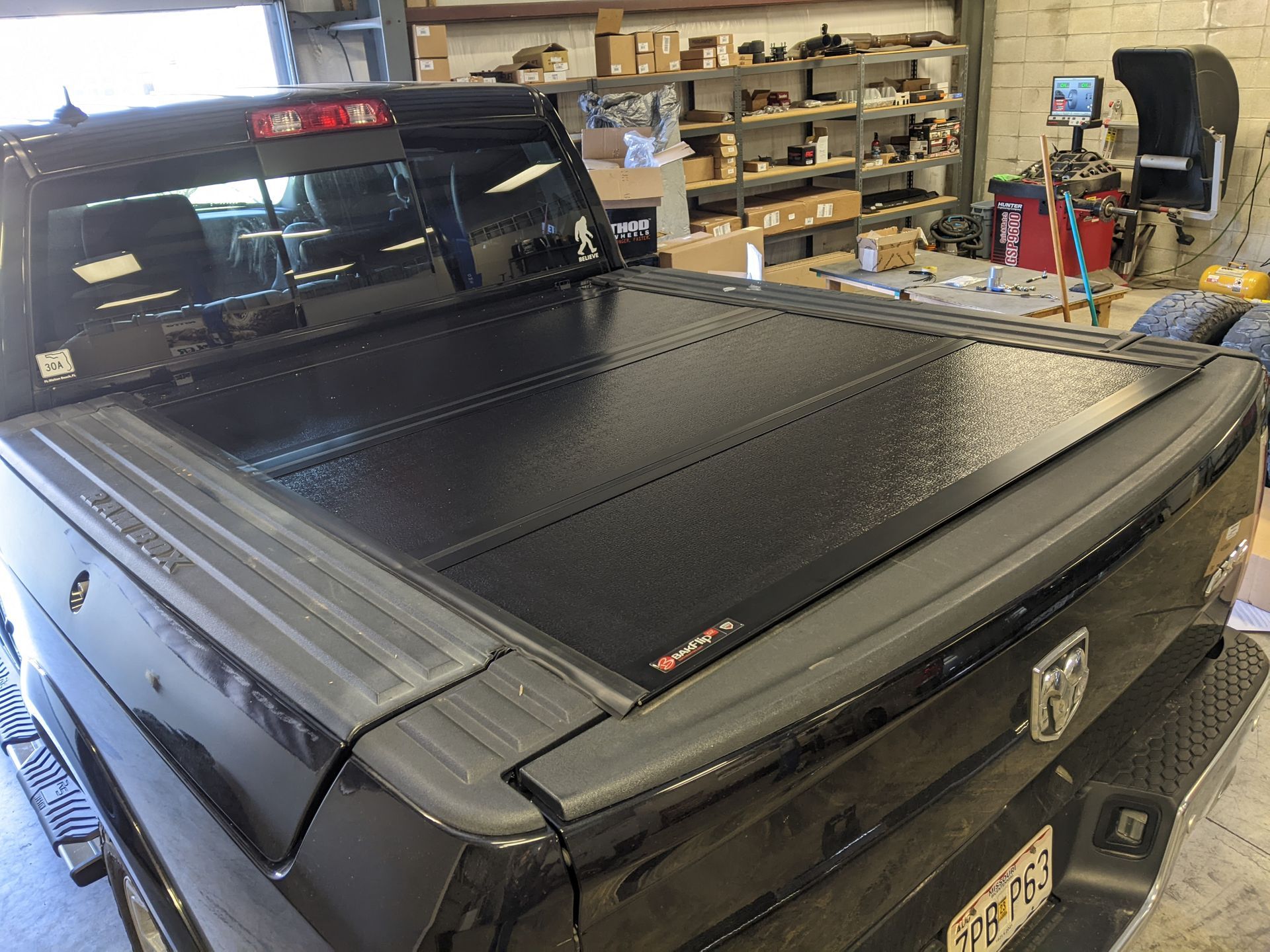 Black pickup truck with a closed tonneau cover parked inside a garage or workshop.