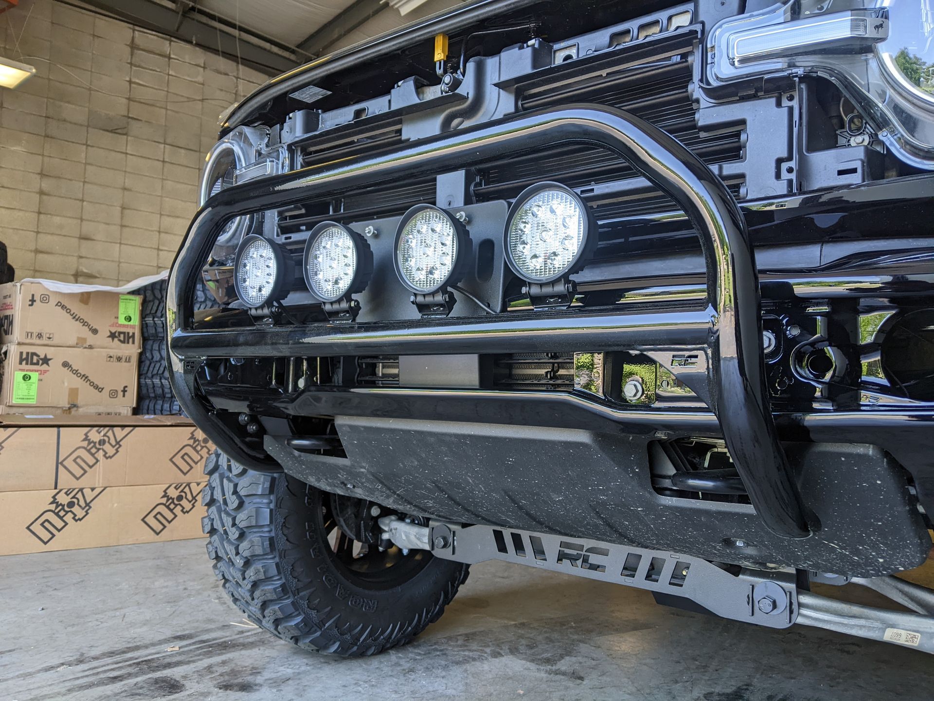 Off-road truck front with four round lights and a heavy-duty black bumper in a garage