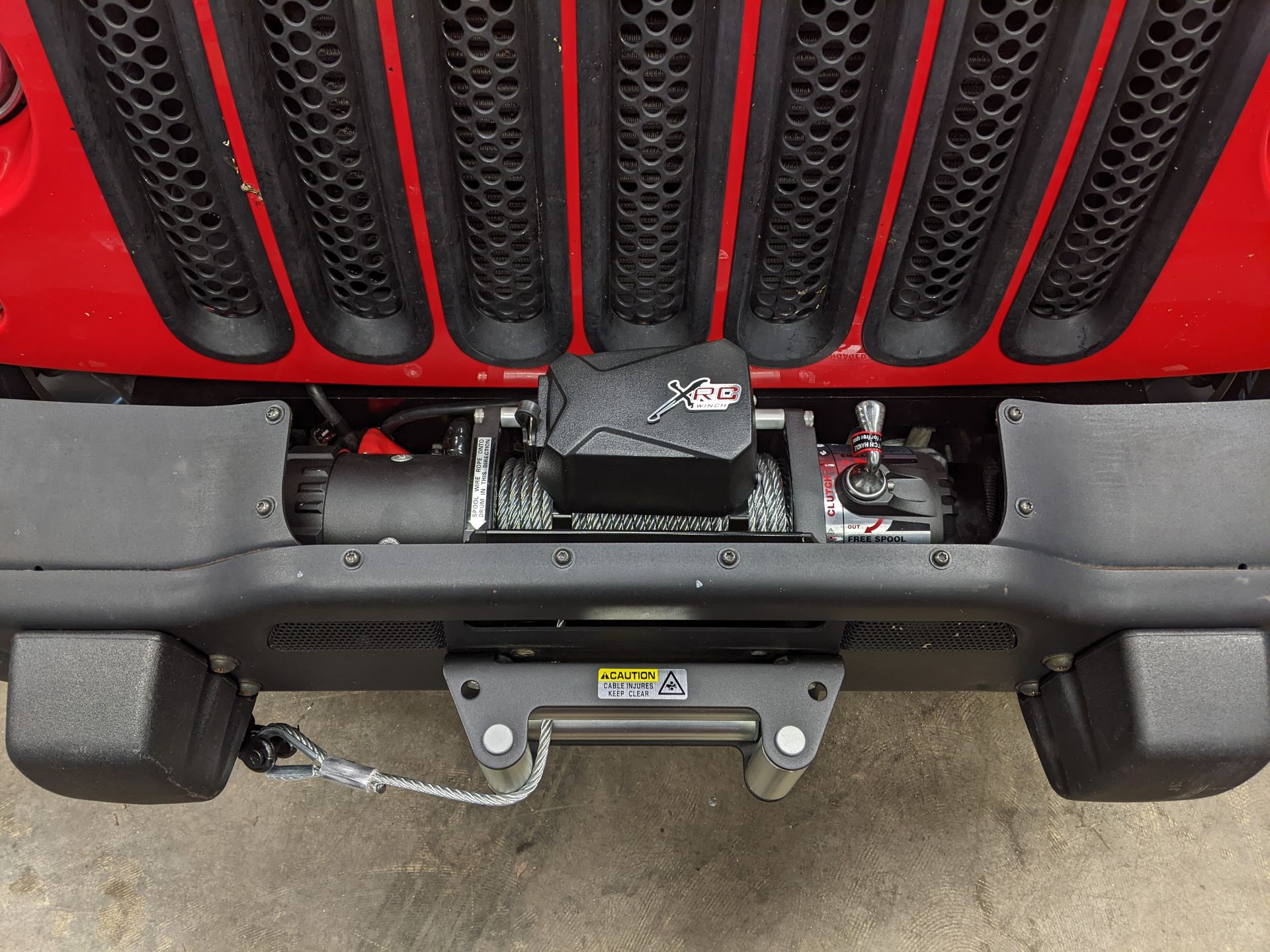 Front view of a red Jeep’s grille, bumper, and winch mounted above a trailer hitch.
