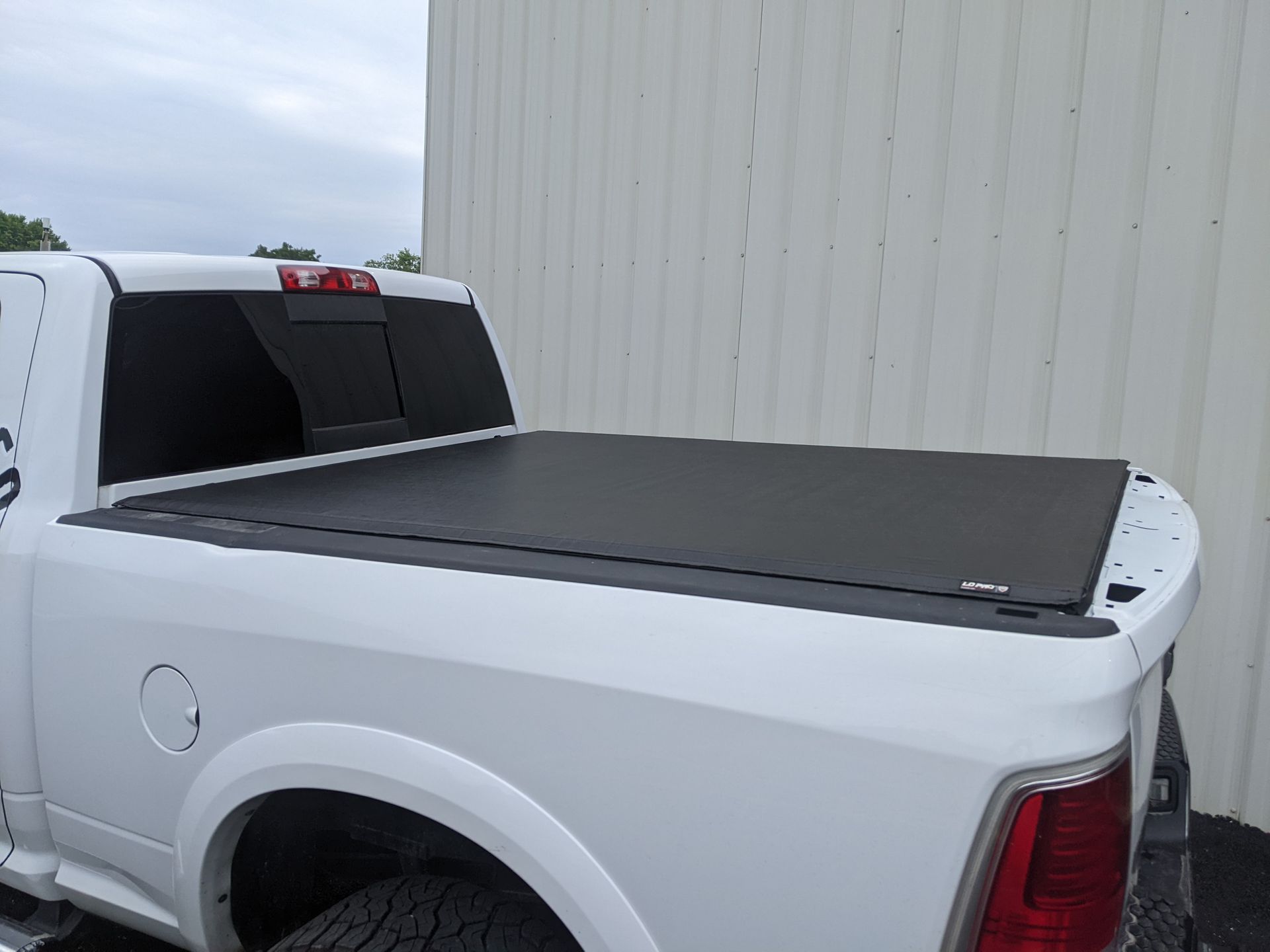 White pickup truck with a black tonneau cover parked beside a corrugated metal wall