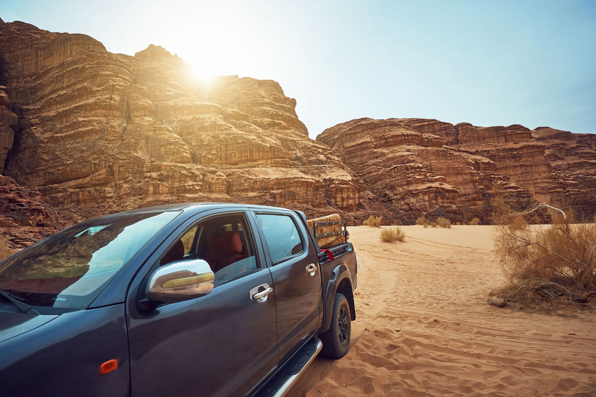 Blue pickup truck driving through a sandy canyon at sunset