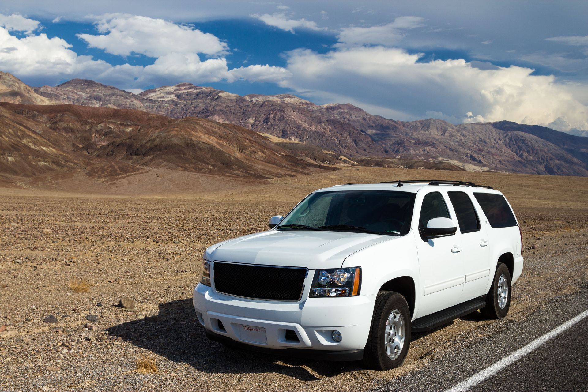 White SUV parked on a desert roadside with mountains and cloudy sky in the background