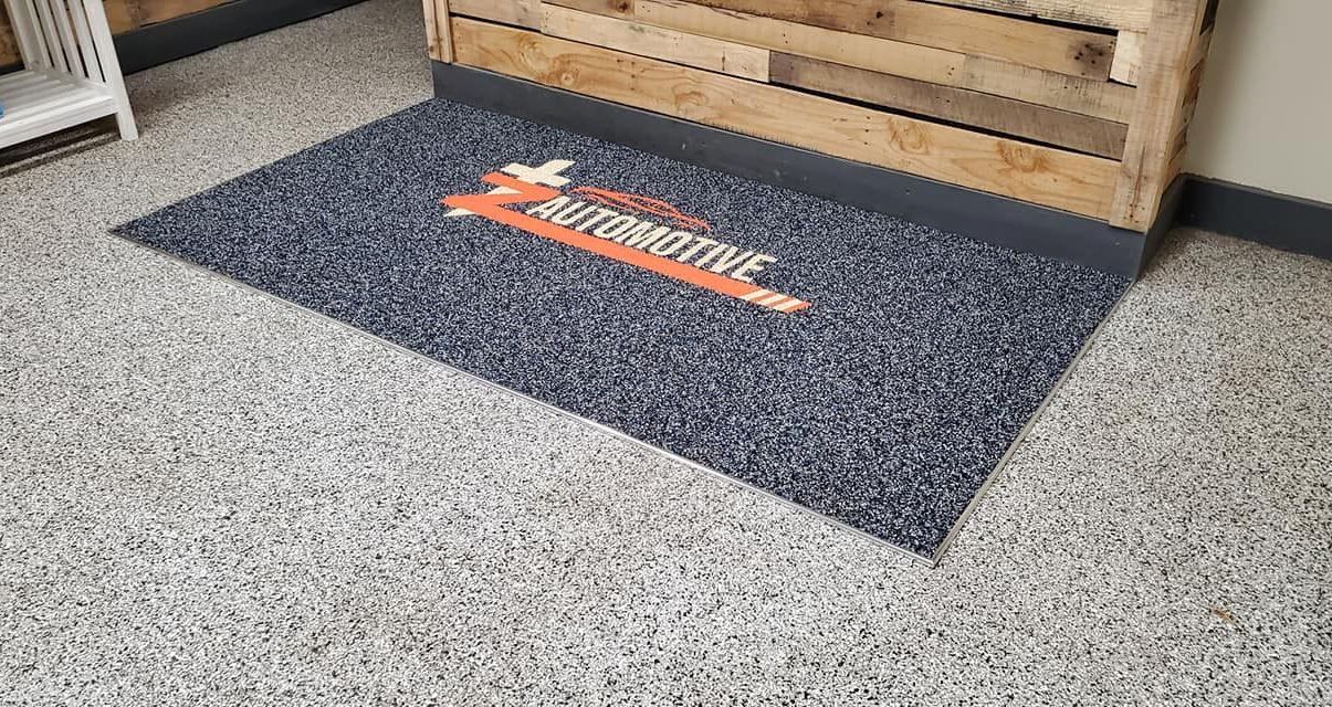 A door mat is sitting on a concrete floor next to a wooden box.