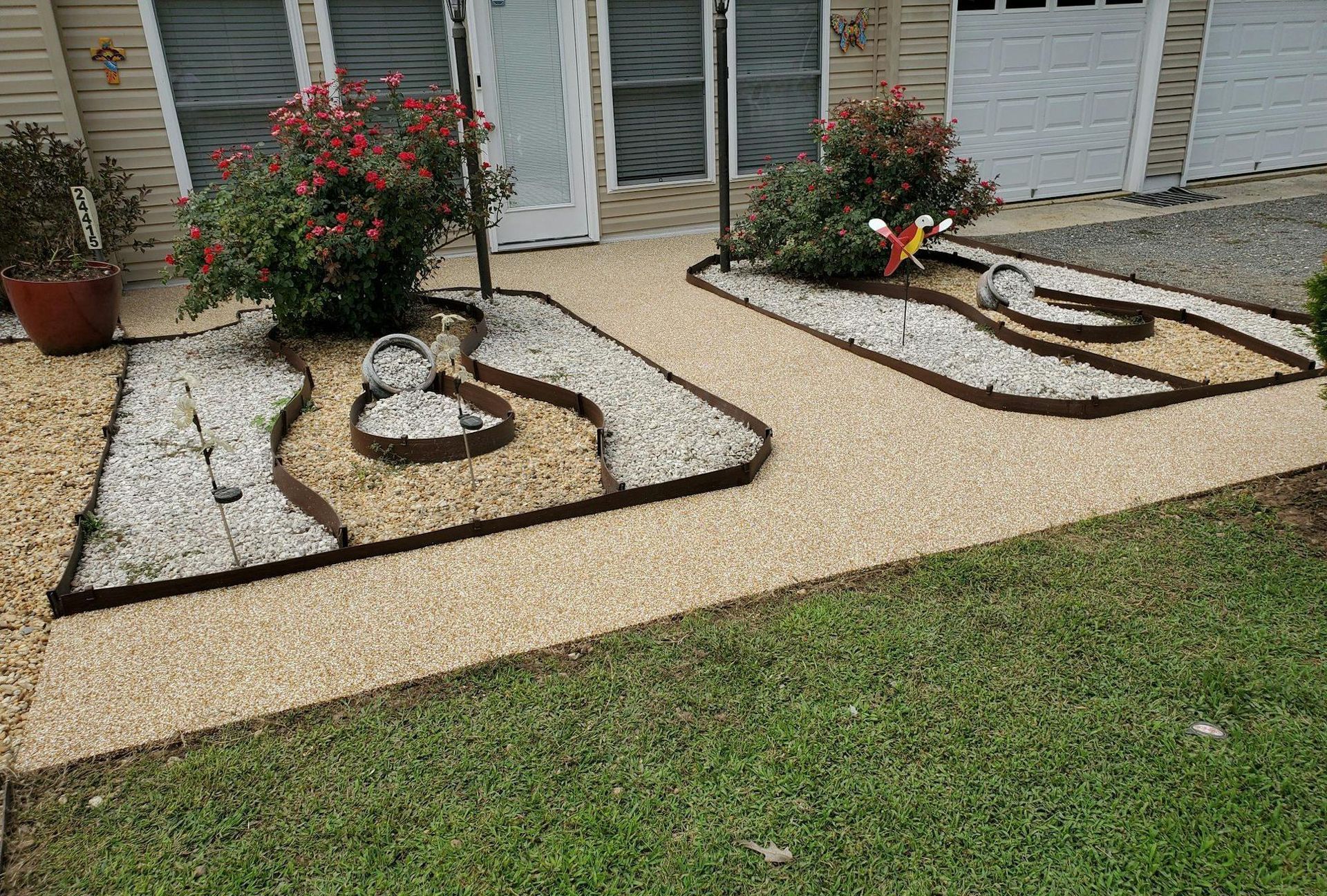 A walkway with gravel and flowers in front of a house.