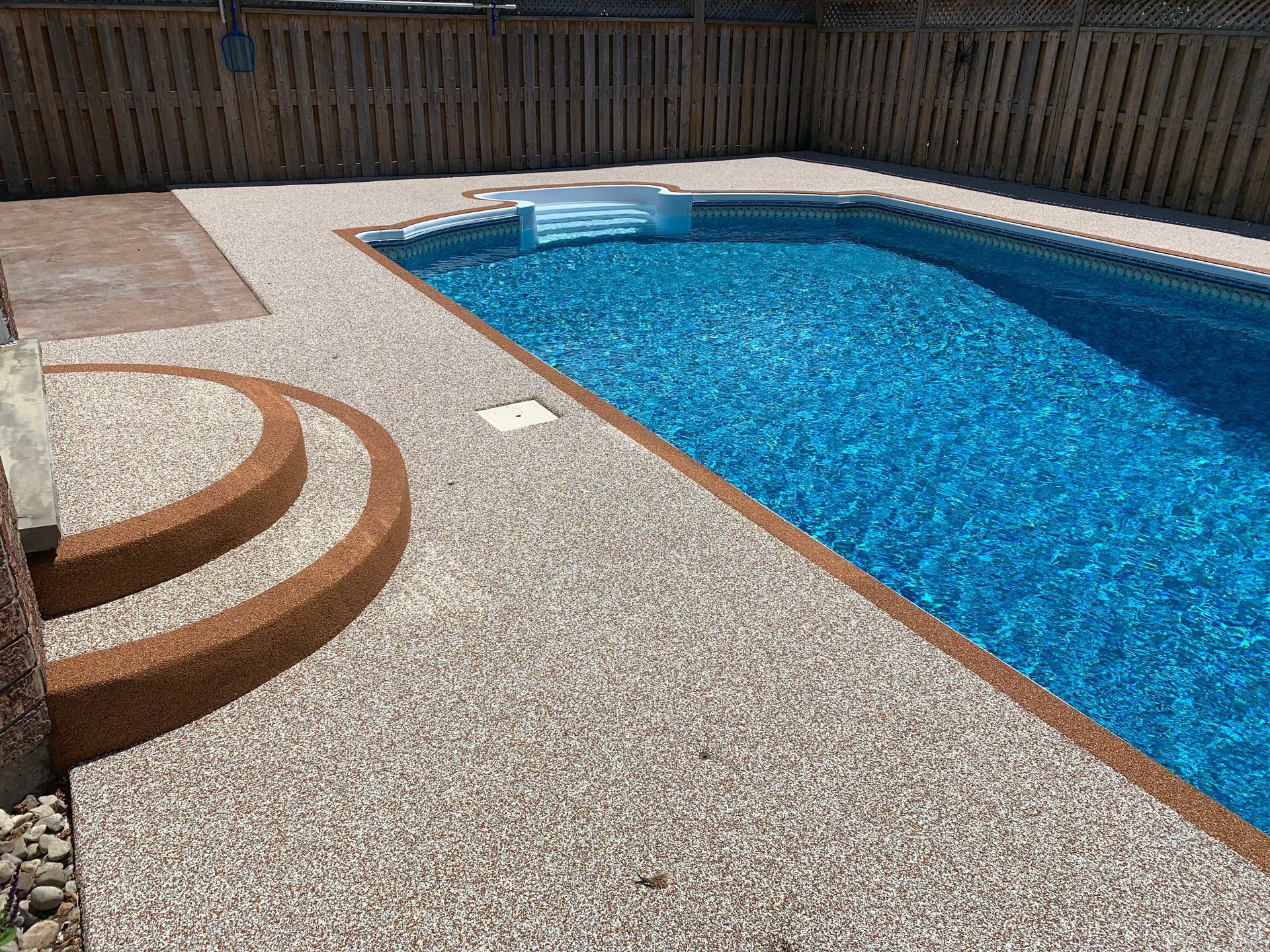 A large swimming pool with stairs leading to it and a wooden fence surrounding it.