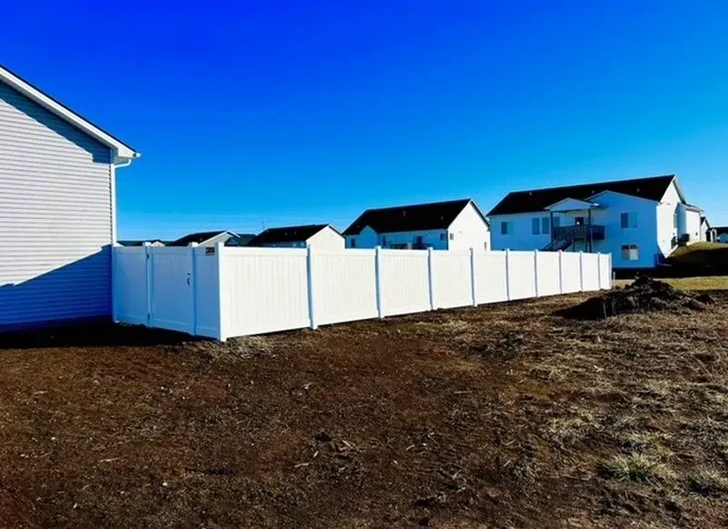 White vinyl fence surrounding a house with other houses in the background on a clear, sunny day.