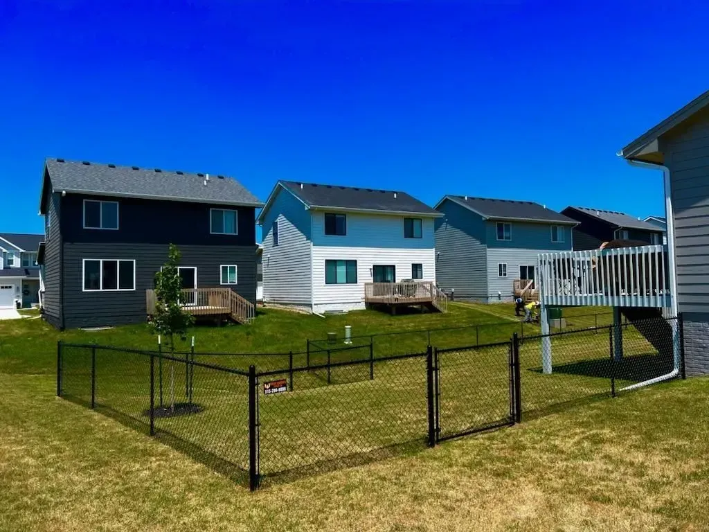 Backyards of three houses with chain-link fence on a bright, sunny day.