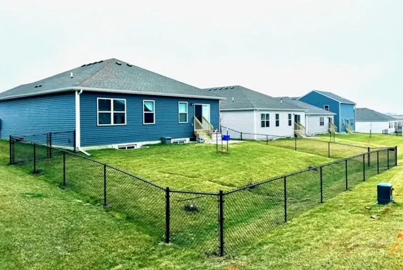 A row of houses with chain link fences in backyards, situated on a grassy hill.