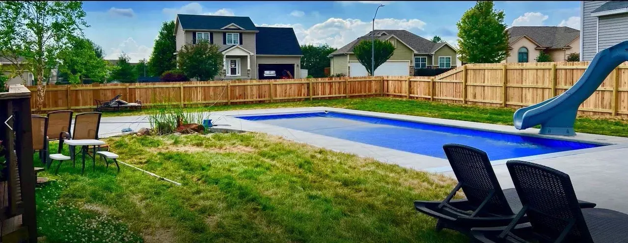 Backyard with a swimming pool, lawn chairs, a slide, and houses in the background.