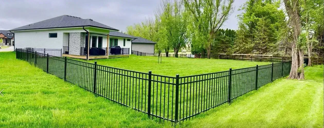 A house with a black metal fence and green lawn. Trees are in the background.