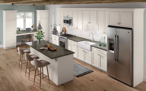 Modern white kitchen with island, bar stools, stainless steel fridge, and large window