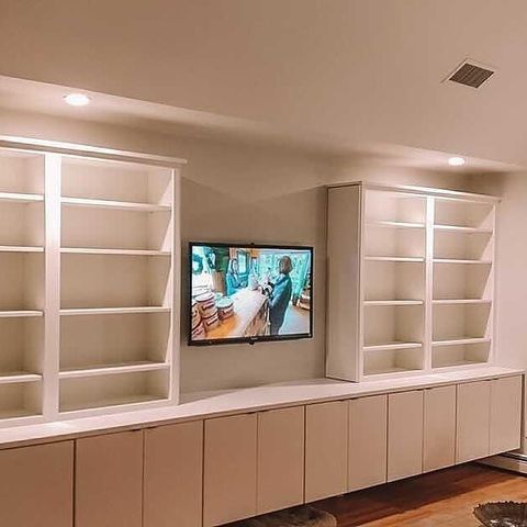 Wall-mounted TV between two white built-in shelving units above a long beige cabinet.