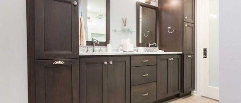 Dark wood double-sink bathroom vanity with mirrors, cabinets, and white countertop in a bright bathroom.