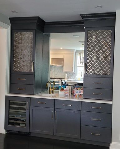 Dark built-in kitchen cabinetry with glass-front shelves framing a pass-through to a bright white kitchen