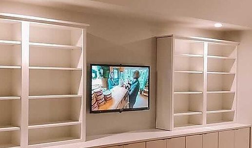 Built-in white shelves framing a wall-mounted TV in a bright, minimalist living room