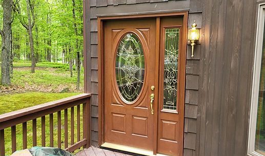 Wooden front door with oval glass panels on a cabin porch, surrounded by green trees