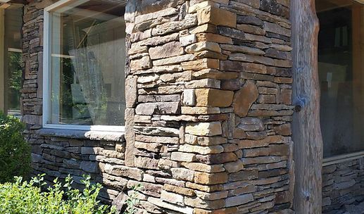 Stone-clad exterior wall with large windows and a wooden post
